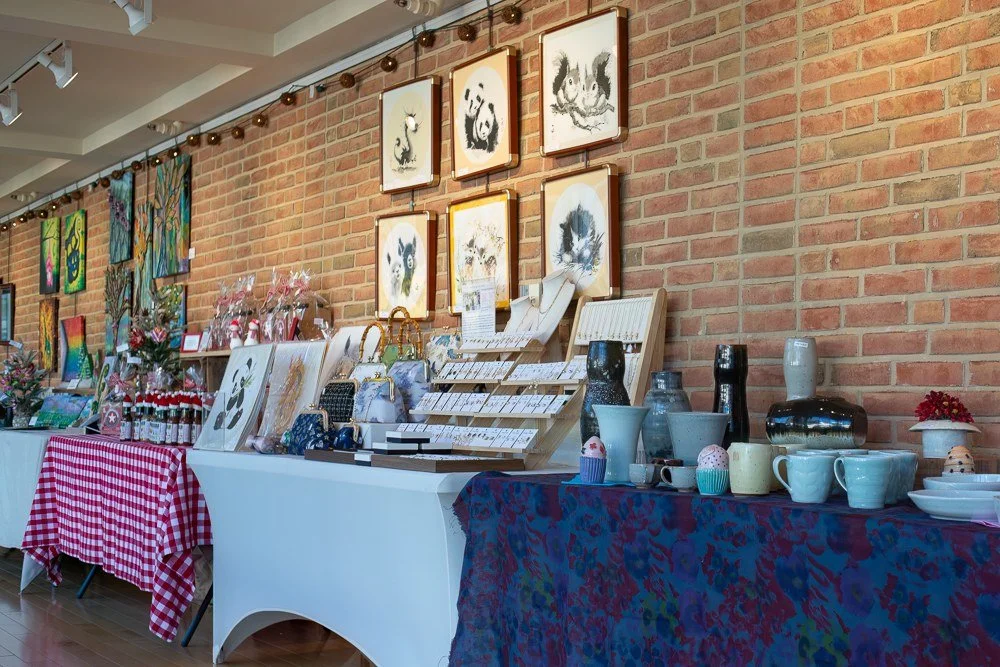 Holiday Gift Show display tables featuring jewelry, ceramics, paintings, and handcrafted gifts.
