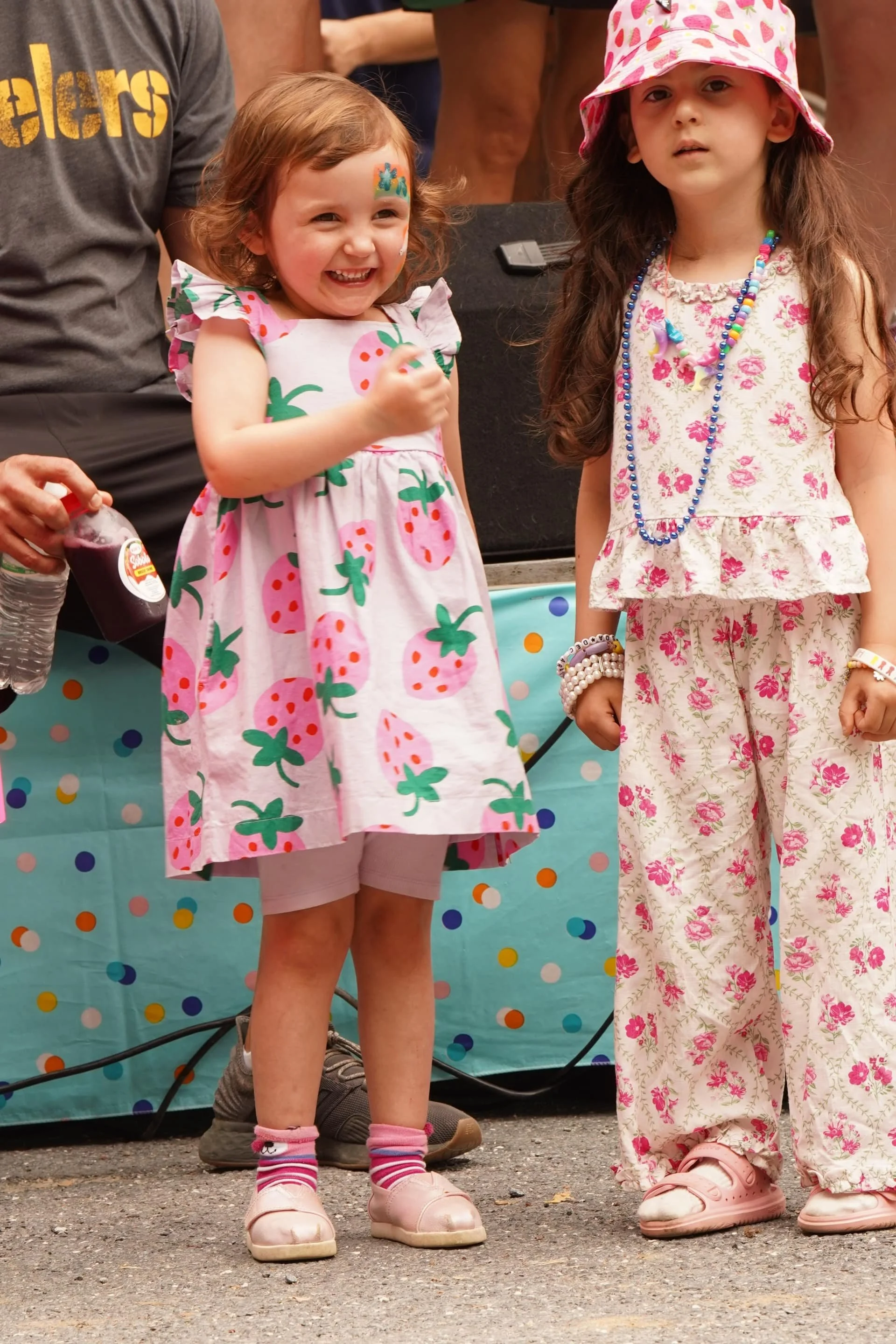 Two children standing on stage in strawberry-themed outfits during a festival activity.