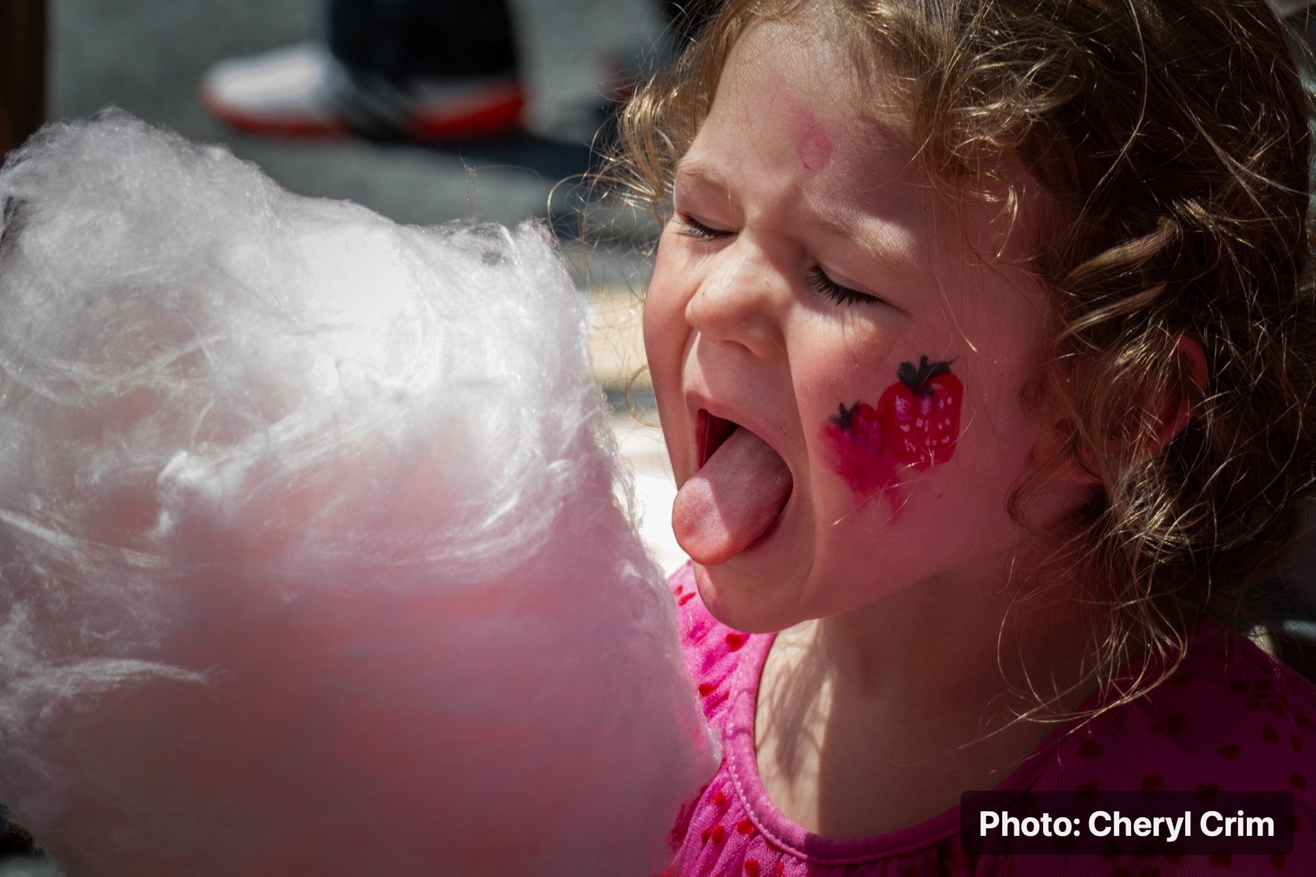 A child smiling while eating cotton candy at the Strawberry Festival.