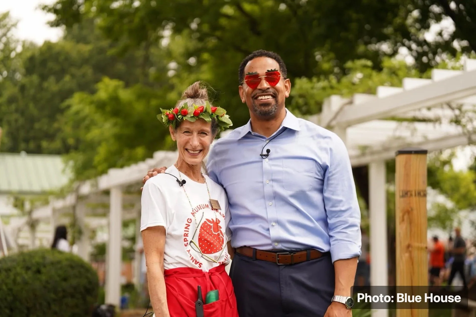 Two people posing together at a community festival with strawberry-themed accessories.