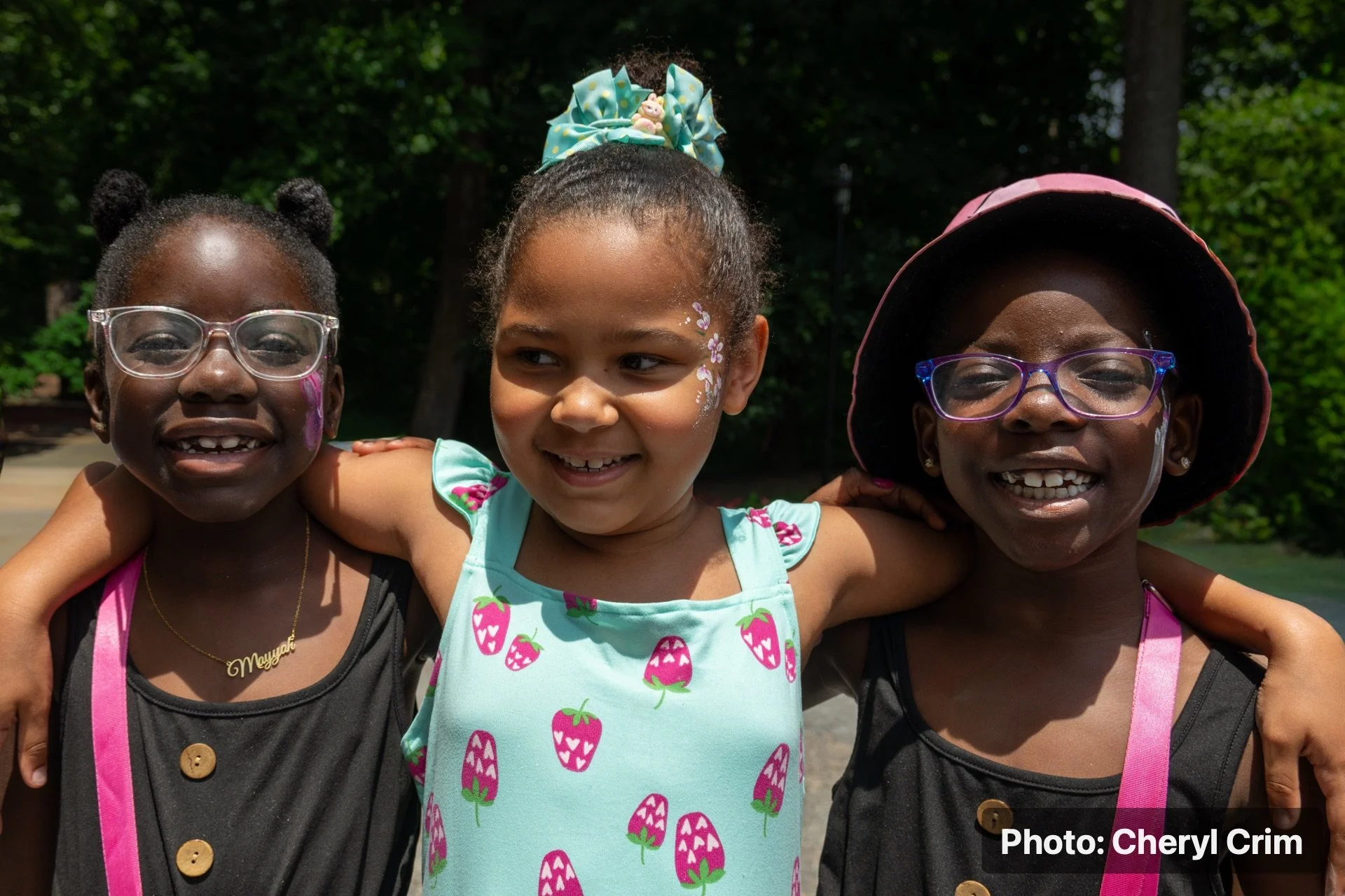 Three smiling children posing together at the Strawberry Festival.