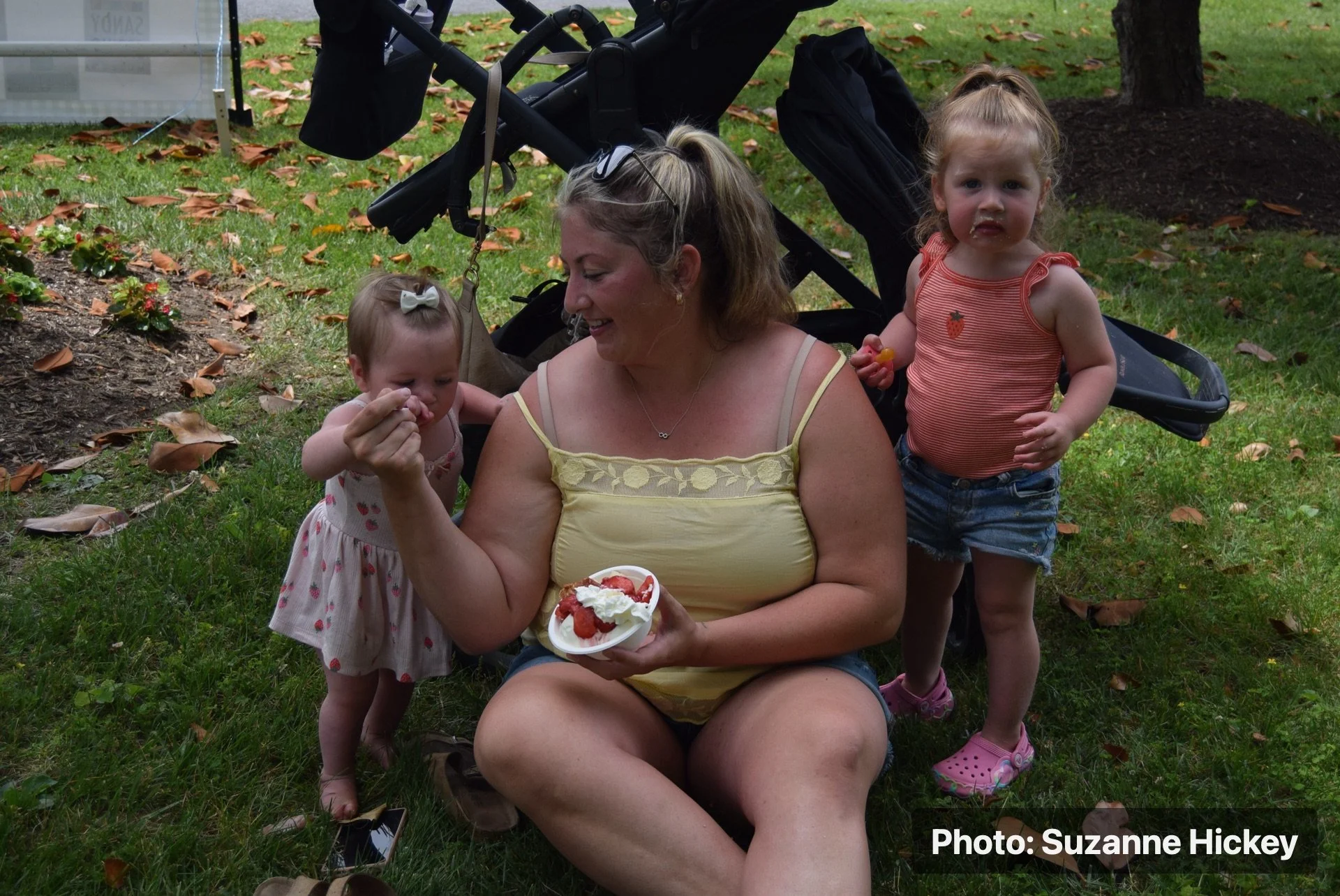 An adult and two children sitting outdoors with strawberry shortcake at the Strawberry Festival.