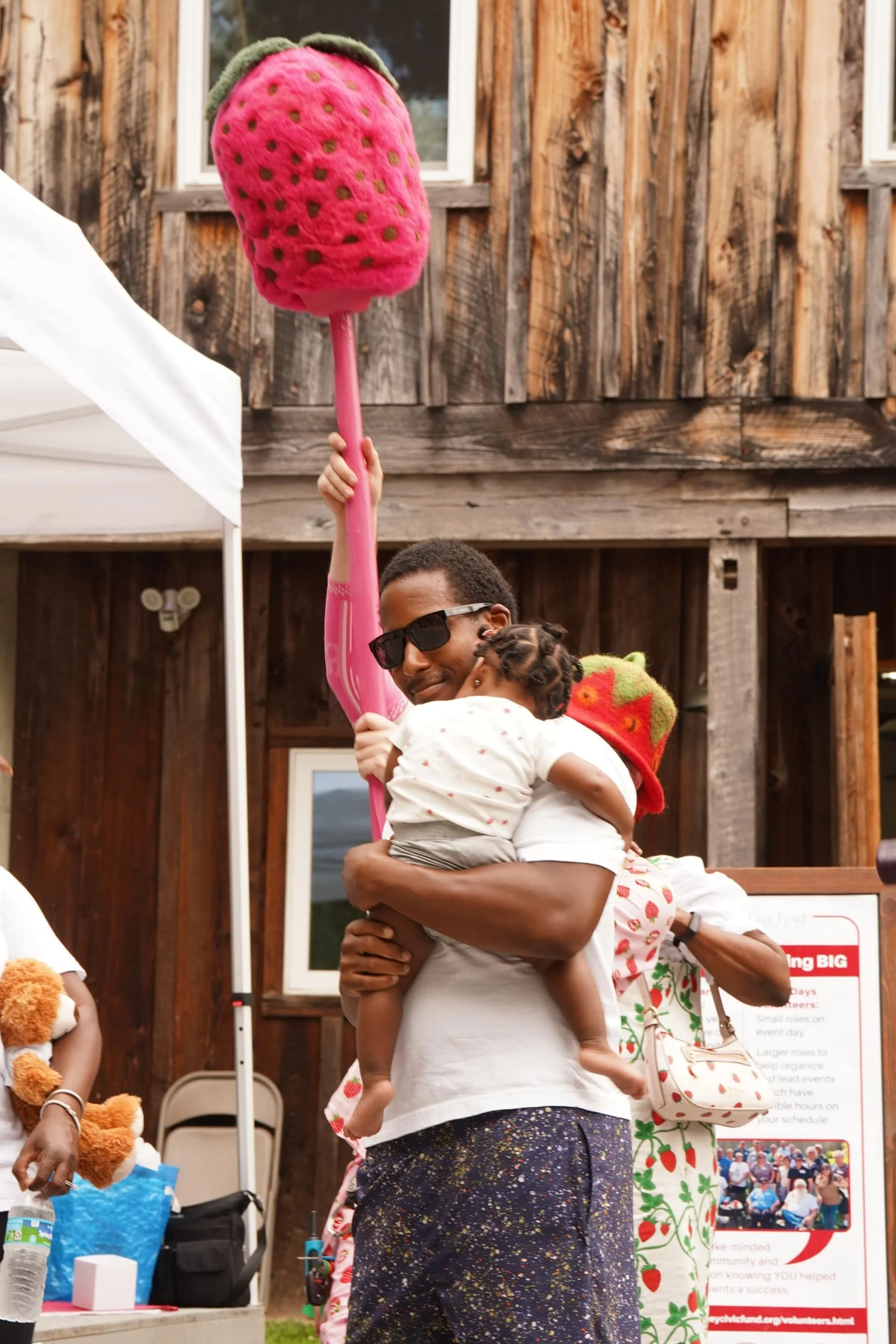 A person carrying a child near a strawberry-themed festival activity area.