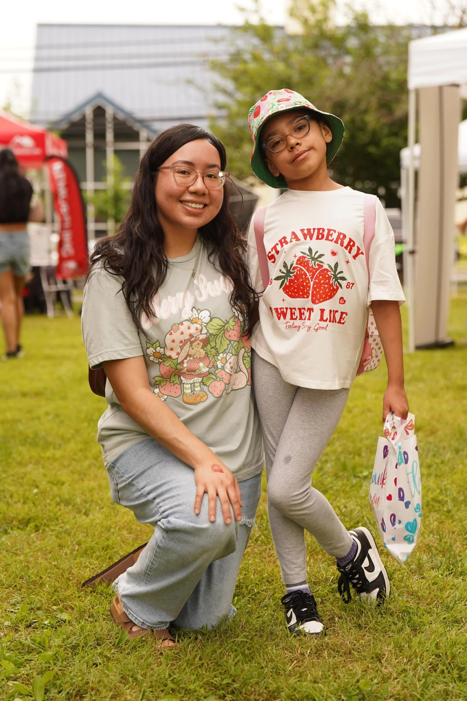 An adult and child posing together at a strawberry-themed community festival.