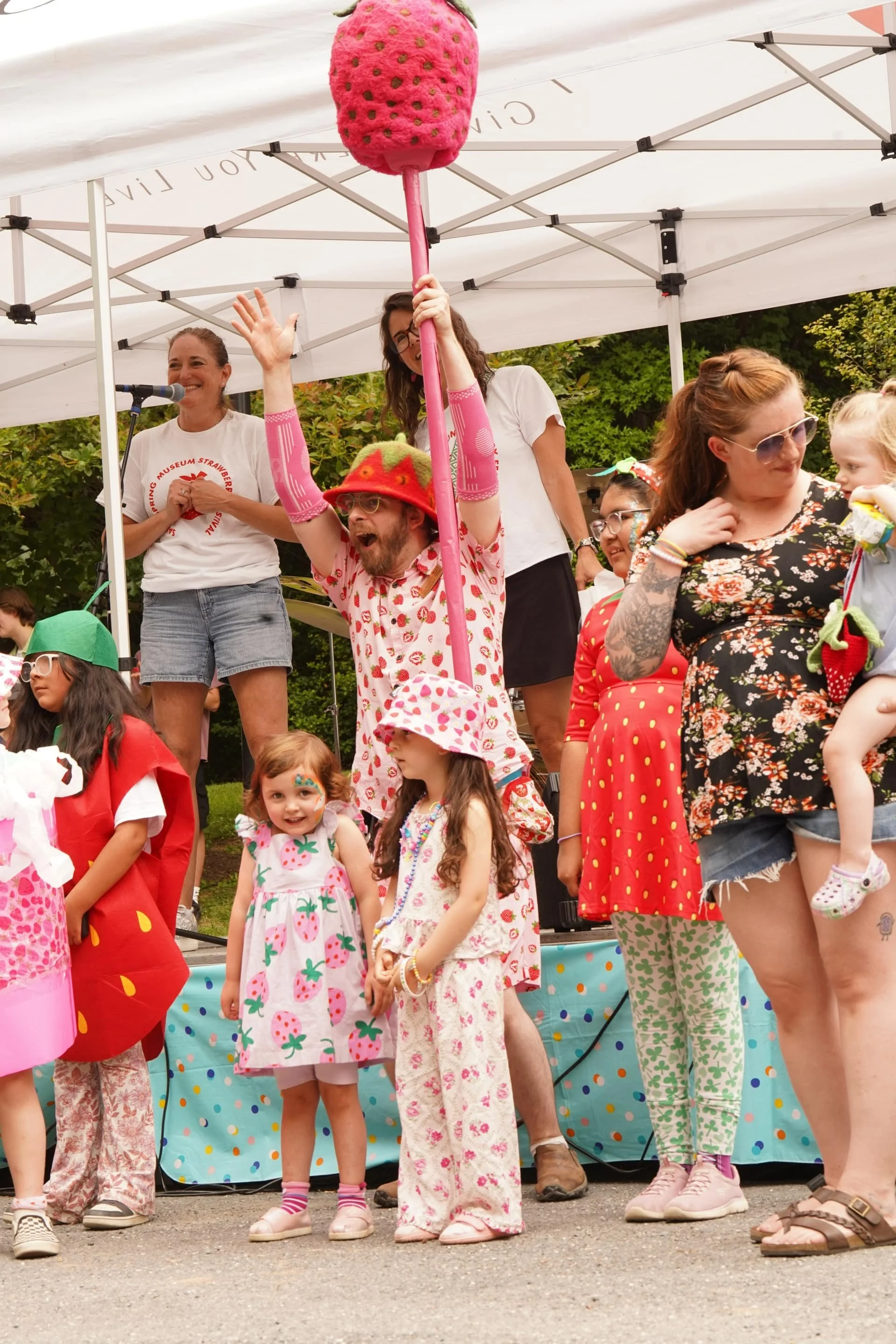Children and families participating in a strawberry-themed costume activity on an outdoor stage.
