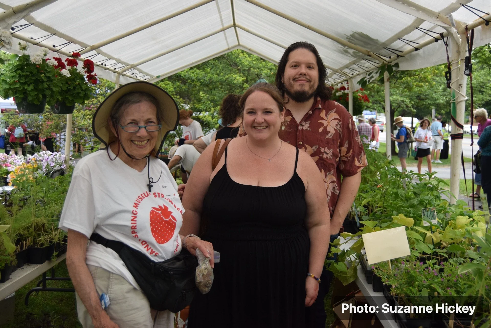Three people posing together in a garden area during the Strawberry Festival.