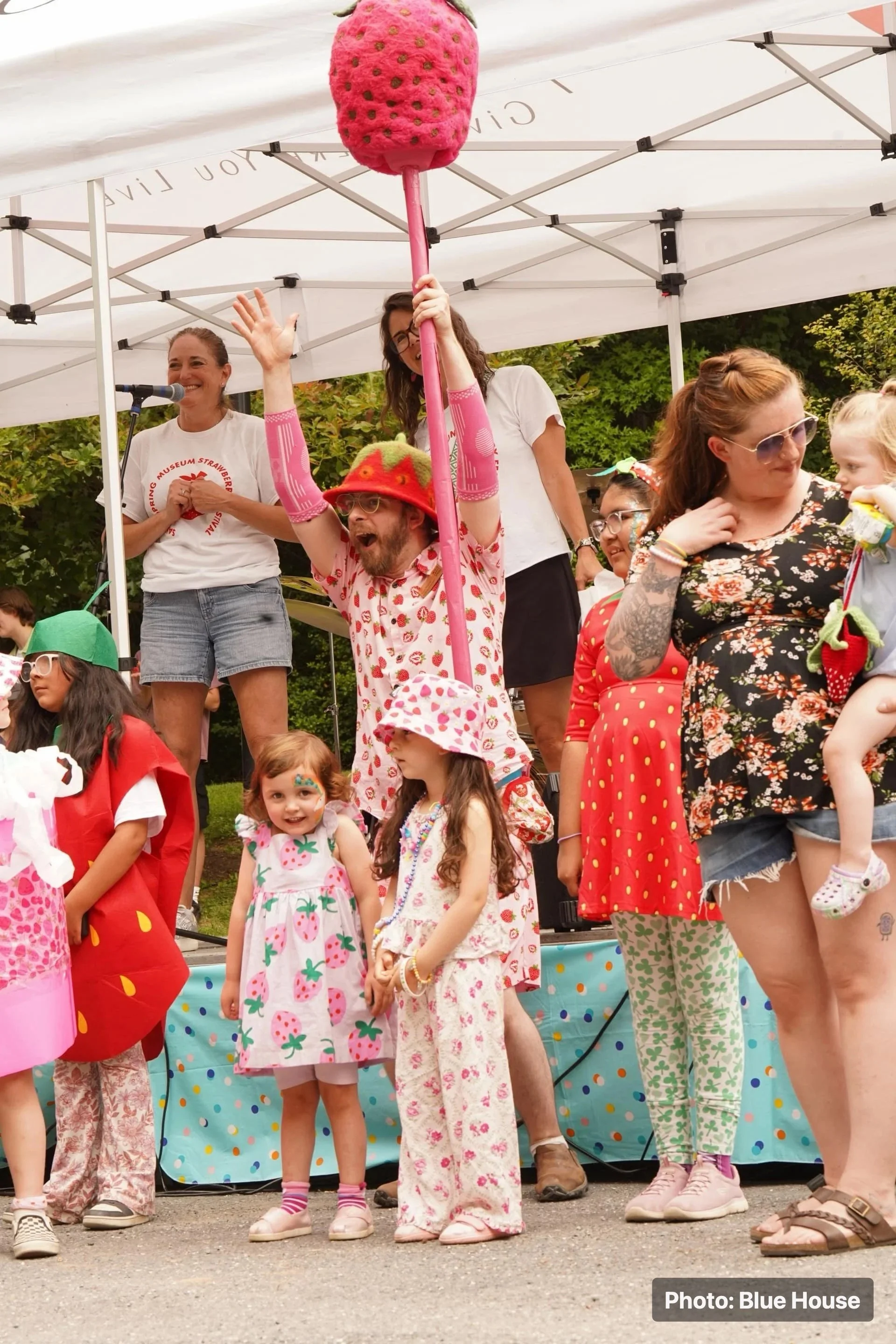 Children and families participating in a strawberry-themed costume activity on an outdoor stage.