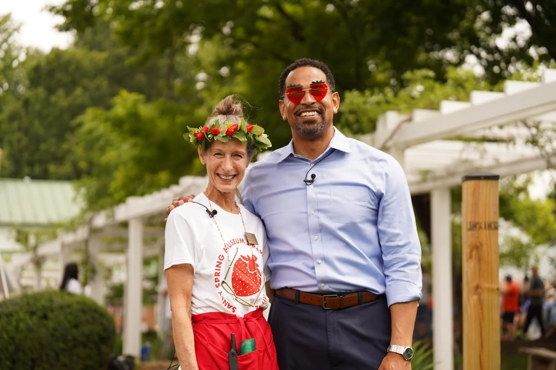 Two people posing together at a community festival with strawberry-themed accessories.