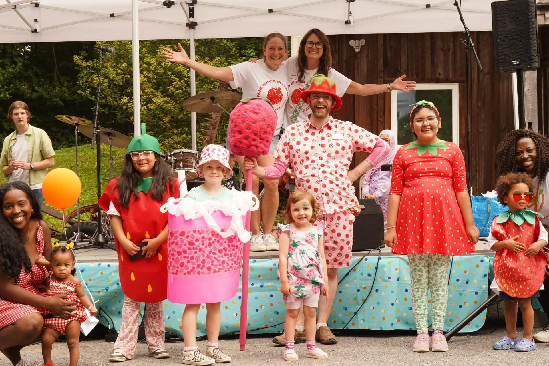 Children and volunteers posing on stage during a strawberry-themed festival costume activity.