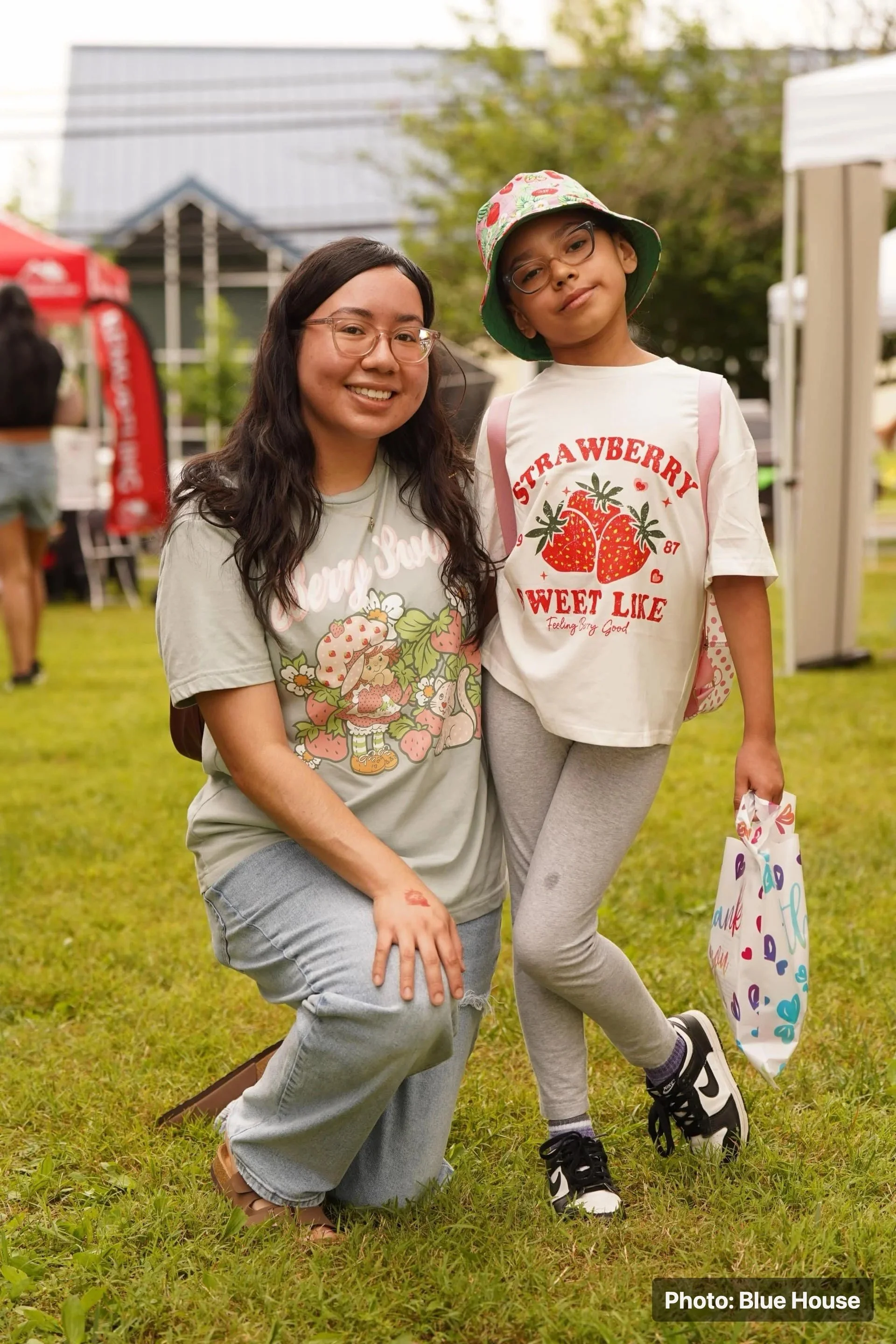 An adult and child posing together at a strawberry-themed community festival.
