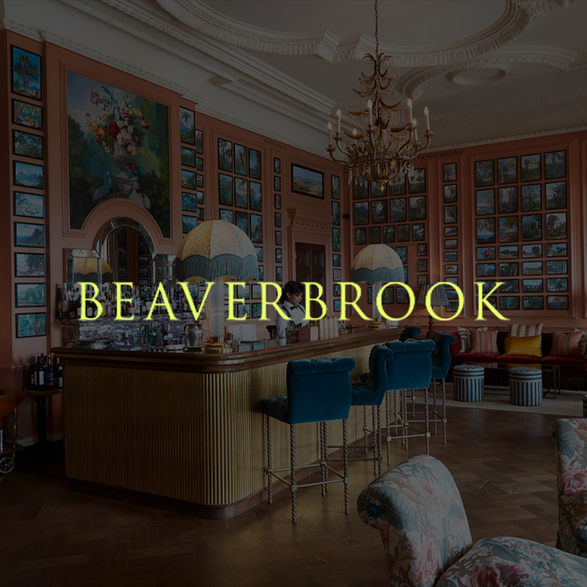 Elegant bar inside a lavish, vintage-style room with pink walls, numerous framed pictures, a large chandelier, and plush seating.