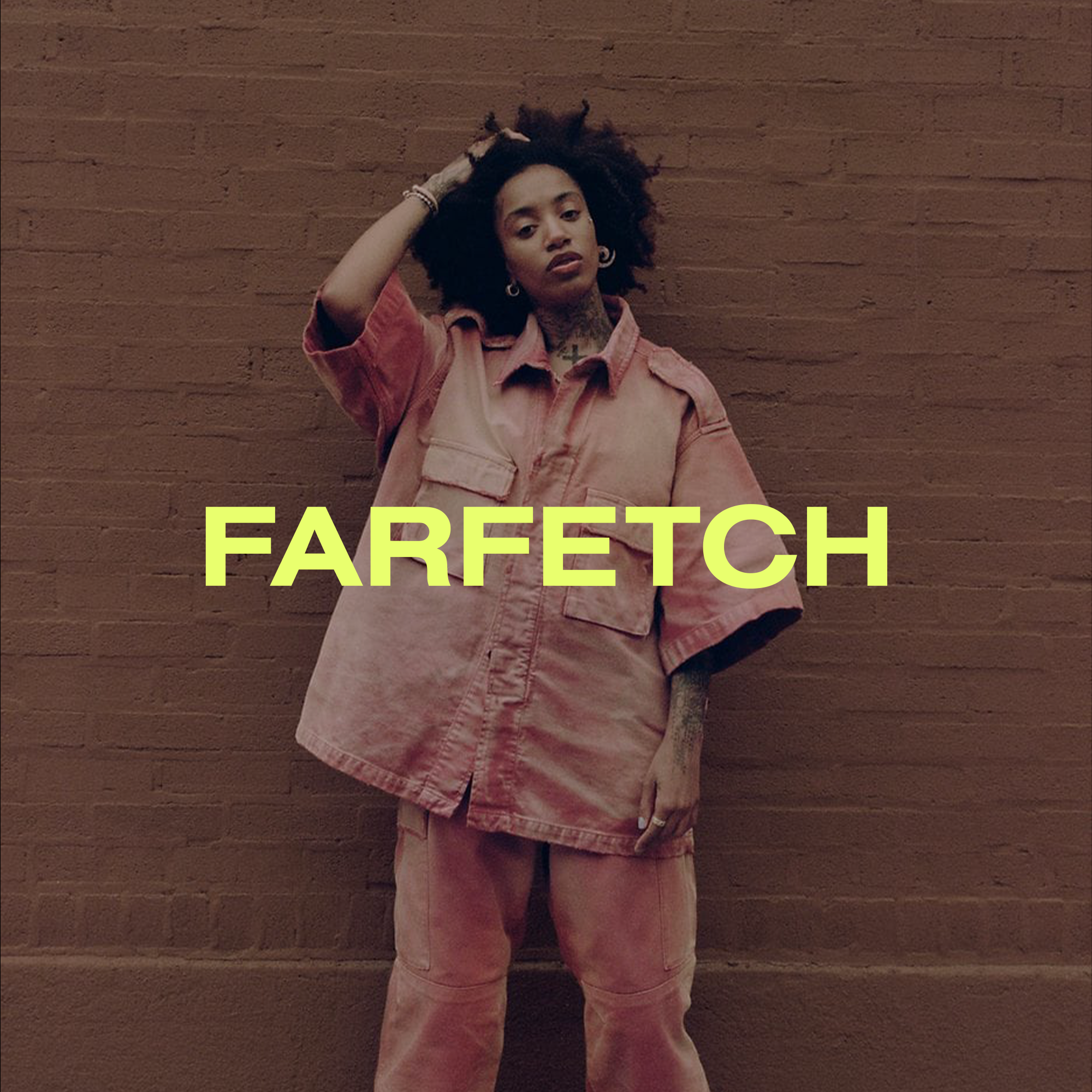 A woman with curly hair standing against a brick wall, wearing a pink oversized shirt and pants, with the word 'FARFETCH' written in bold yellow letters across the image.