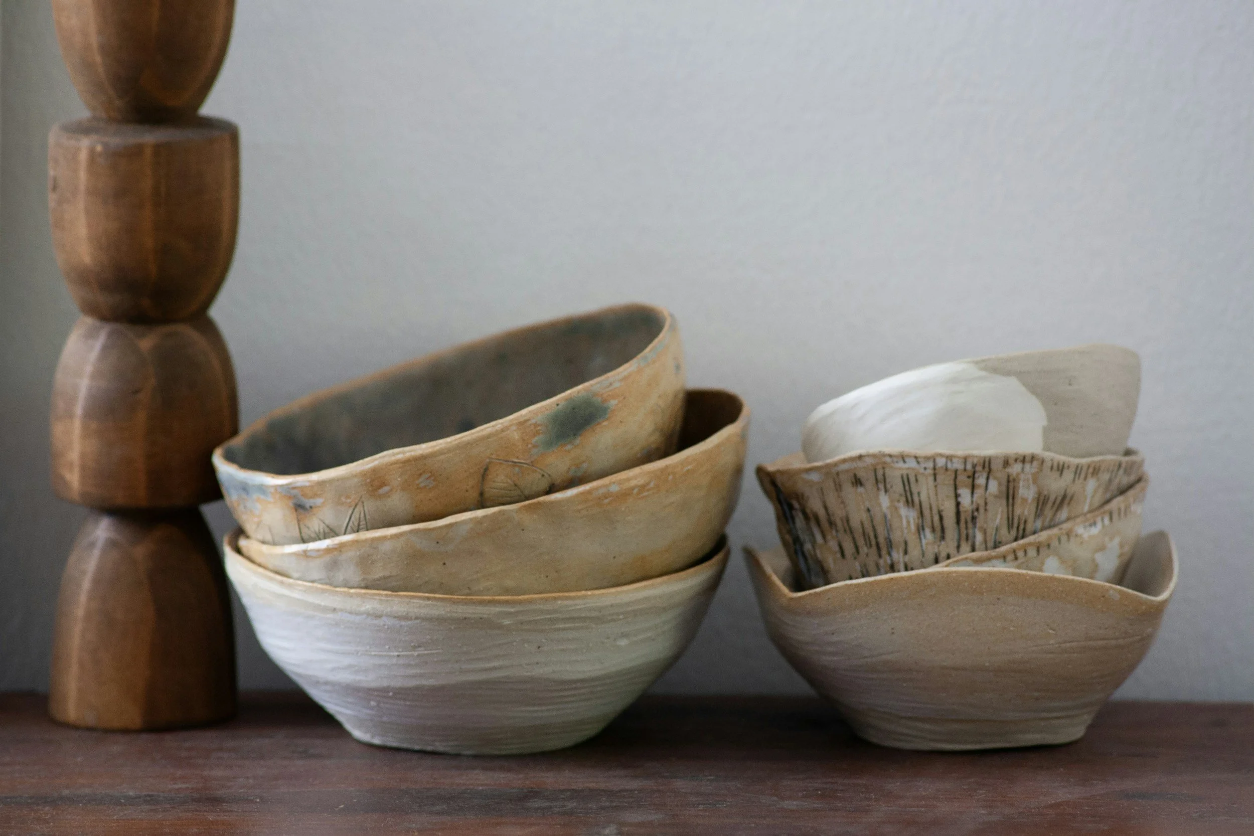 Stacked ceramic bowls on a wooden surface with wooden decorative objects to the left, against a plain wall background.