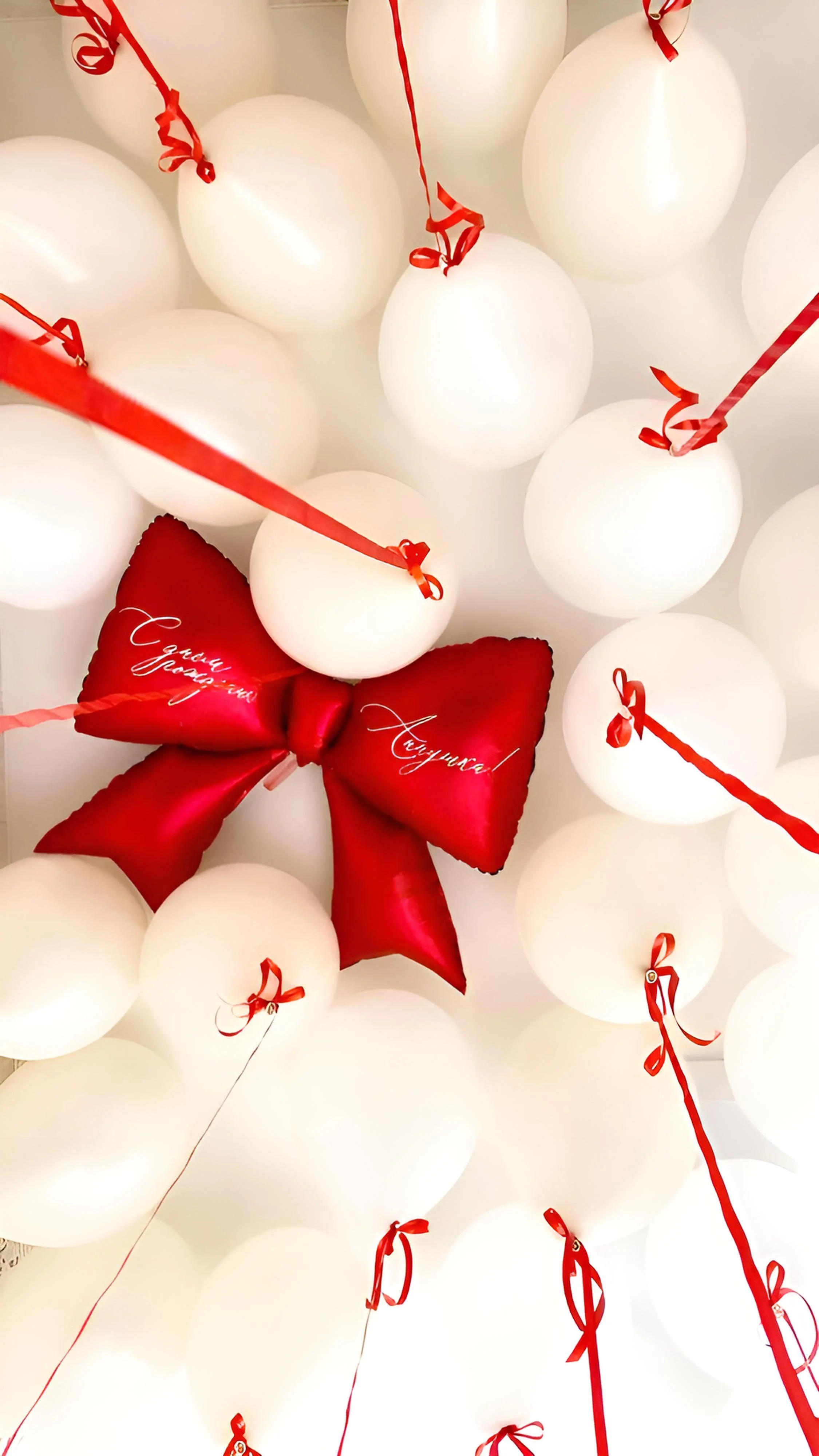White balloons with red ribbons and a red bow with Cyrillic writing on it.