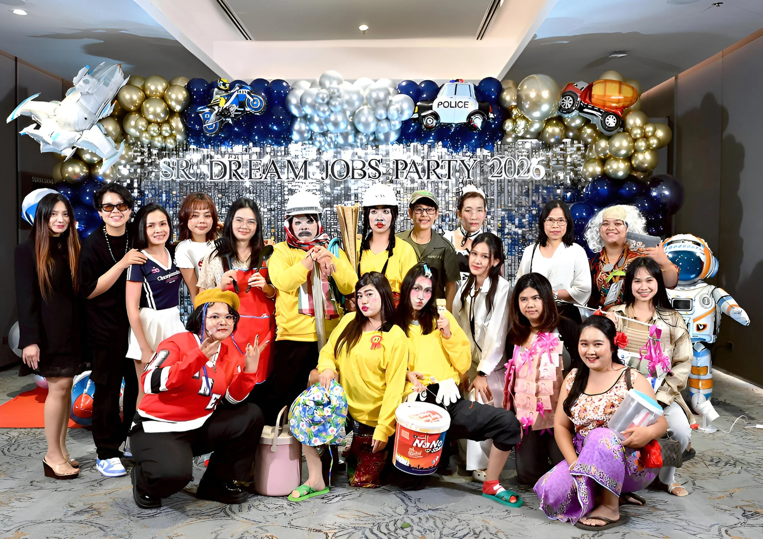 Group of people posing in front of a decoration backdrop with balloons and a sign that reads 'SR. DREAM JOBS PARTY 2026' at a festive event.
