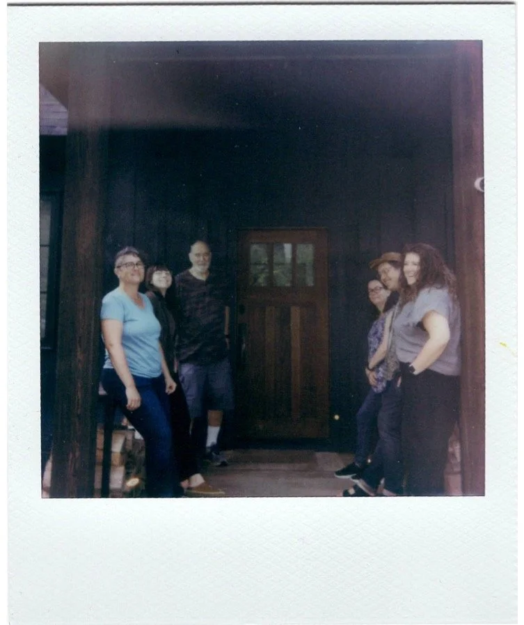 Group of five people standing on a porch in front of a dark wooden door, posing for a photo.