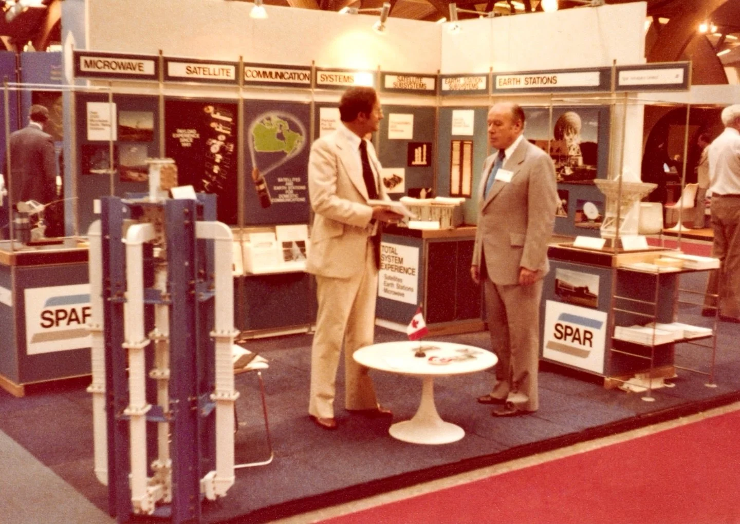 Total System Experience

Ireal is seen here talking to a colleague at the Spar Aerospace booth at an industry convention or tradeshow. Judging by the satellite diagrams on the left, most likely in 1979-1980. 

One can observe Spar advertising its man