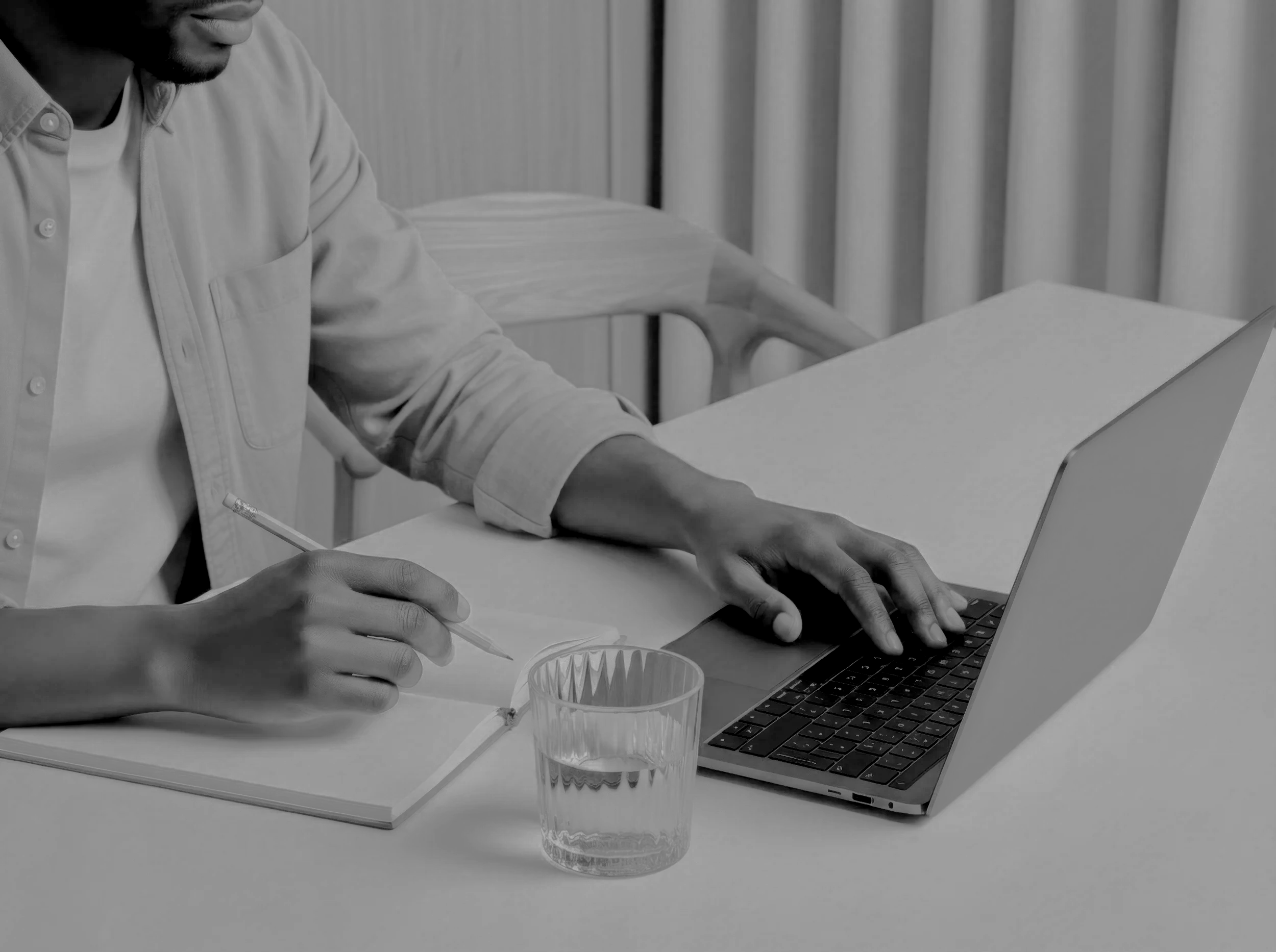 Man working on a laptop while taking notes in a notebook