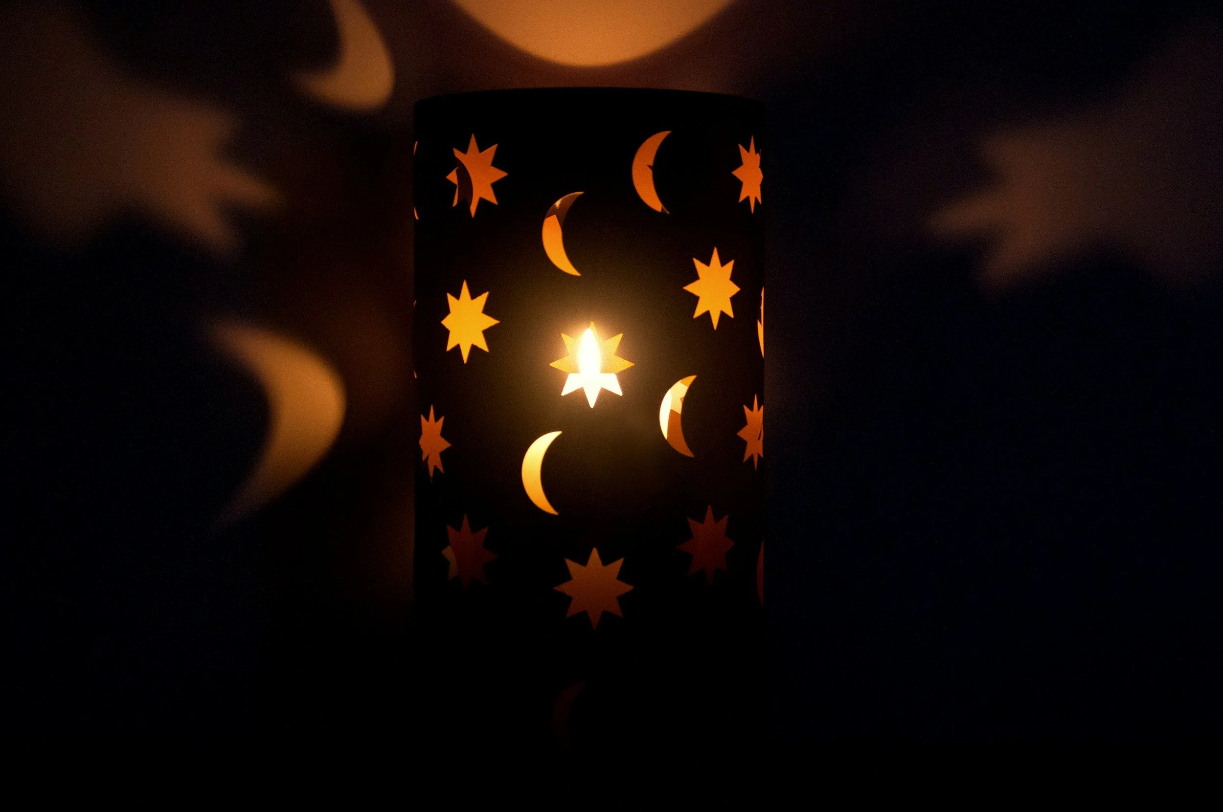 A candle holder with moon and star cutouts emitting a warm glow in darkness.
