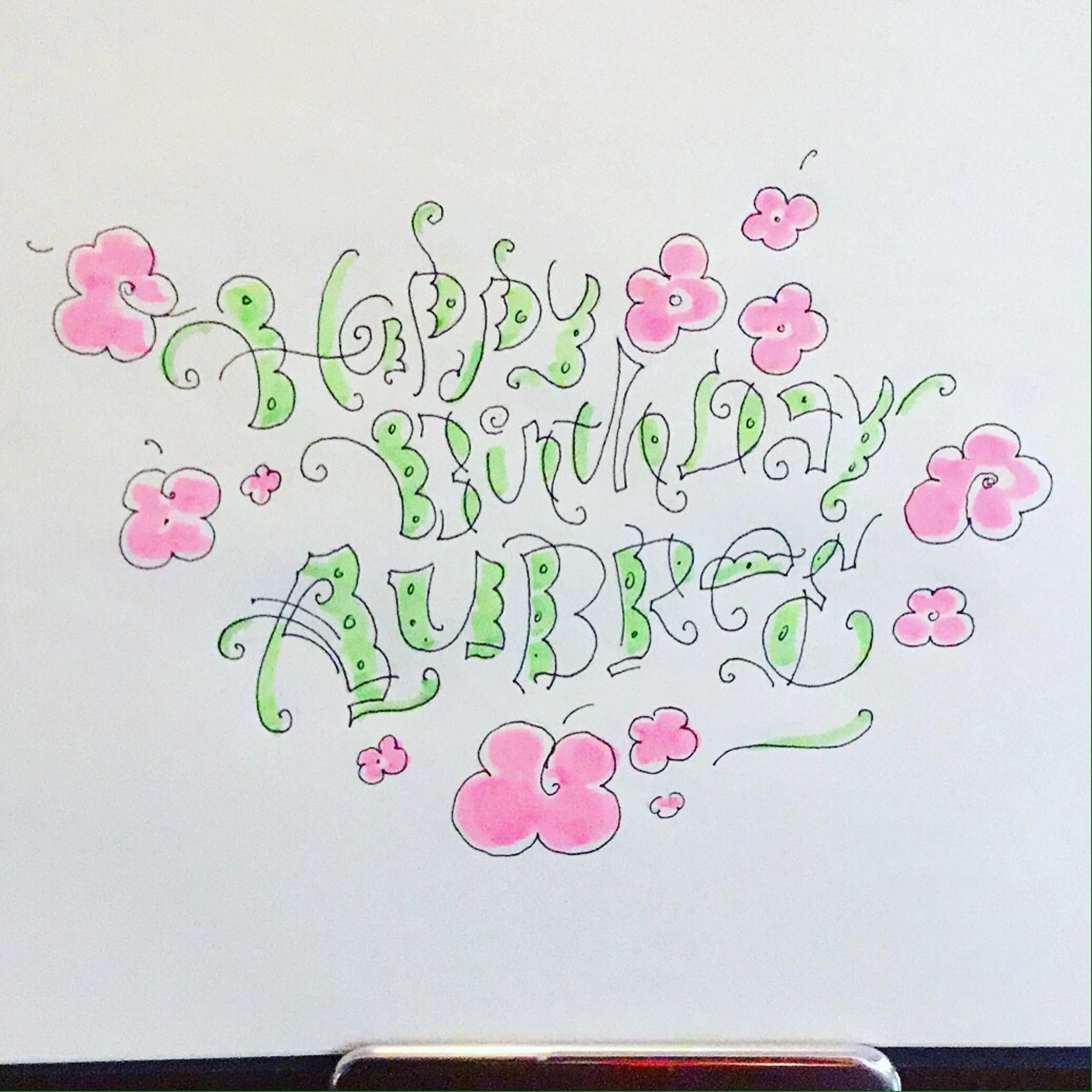 Colorful "Happy Birthday Aubrey" hand-drawn text with pink flowers on a white background.