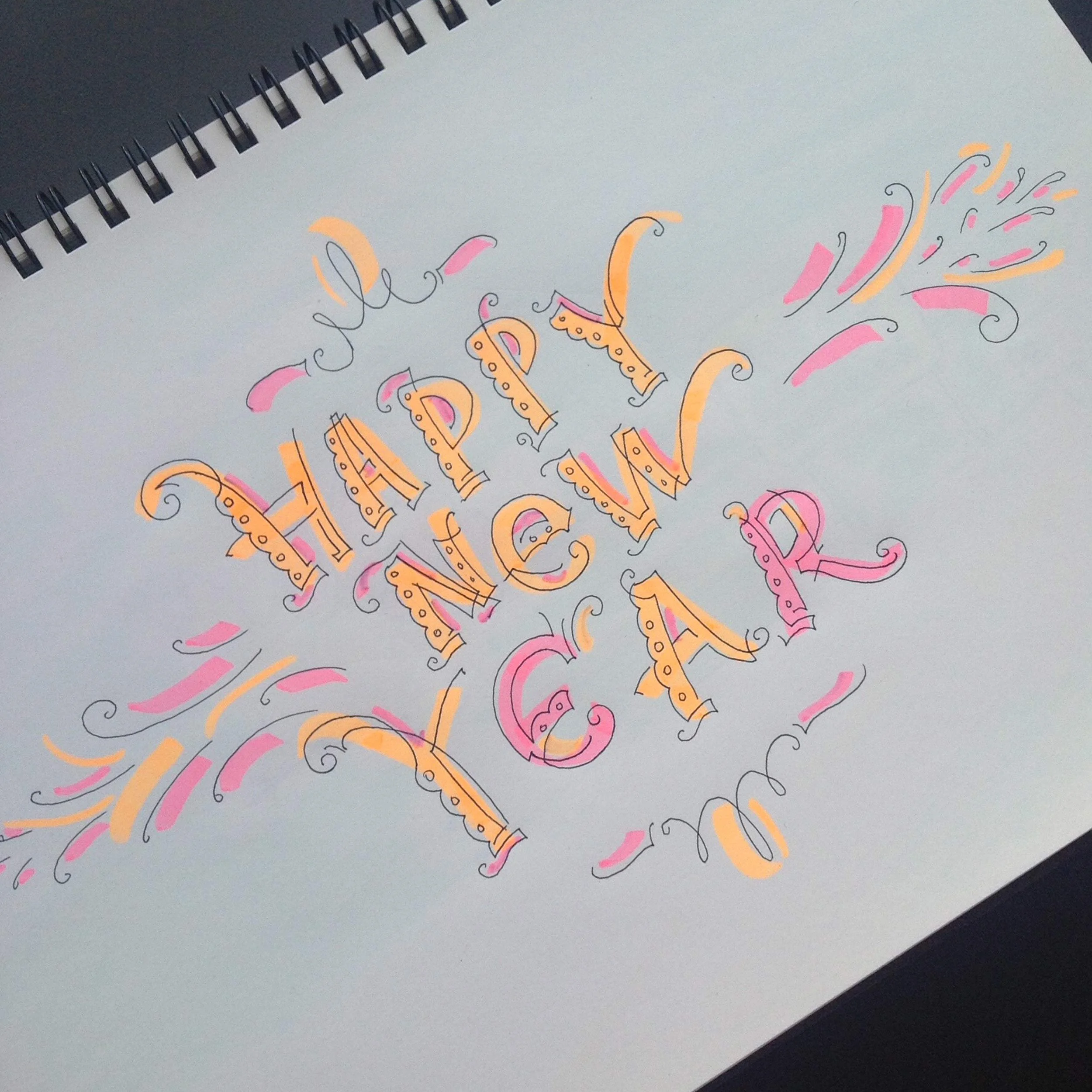 Colorful hand-drawn "Happy New Year" lettering on a sketchpad, decorated with swirls and flourishes in pink and orange.