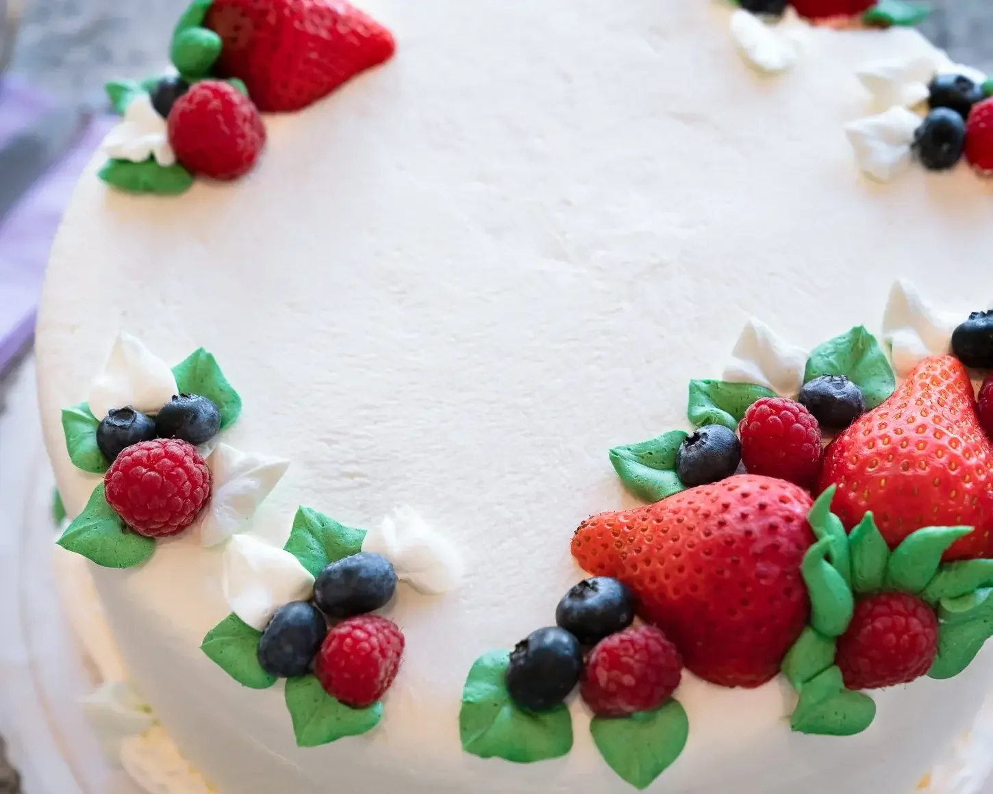 A close-up of a signature white frosted cake decorated with fresh strawberries, raspberries, and blueberries, available for bakery pre-order at Lilac Montecito.
