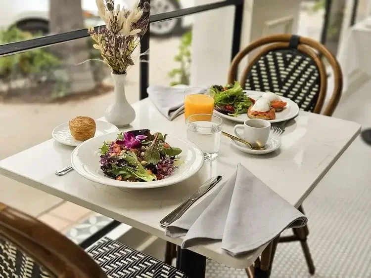 California-style breakfast at Lilac Montecito featuring fresh salads, eggs benedict, and orange juice on an outdoor patio.