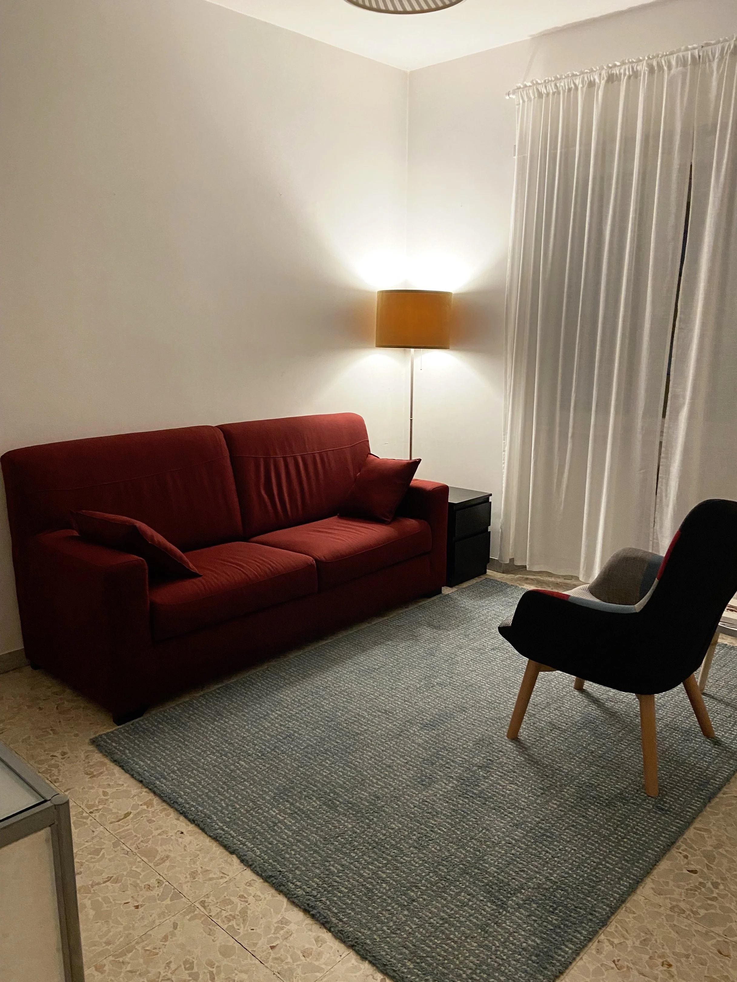 Studio di psicologo a Roma (Colli Albani - Appio Latino) del Dott. Francesco Turco con divano rosso, poltrona patchwork, tappeto azzurro, lampada da terra, tende bianche.