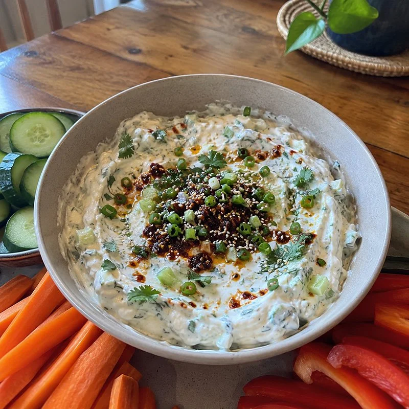 Protein Greek yogurt dip with chili crisp, cucumber, herbs, green onion, sesame seeds, and fresh vegetables on the side.