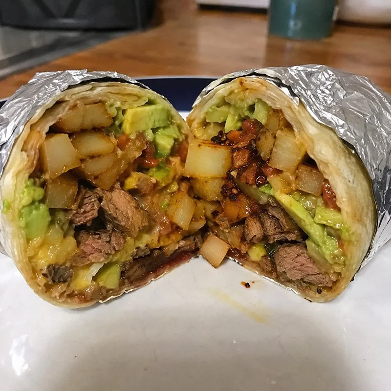 Healthy California burrito with chili crisp, lean steak, roasted potatoes, avocado, cheese, and fresh toppings wrapped in a tortilla.