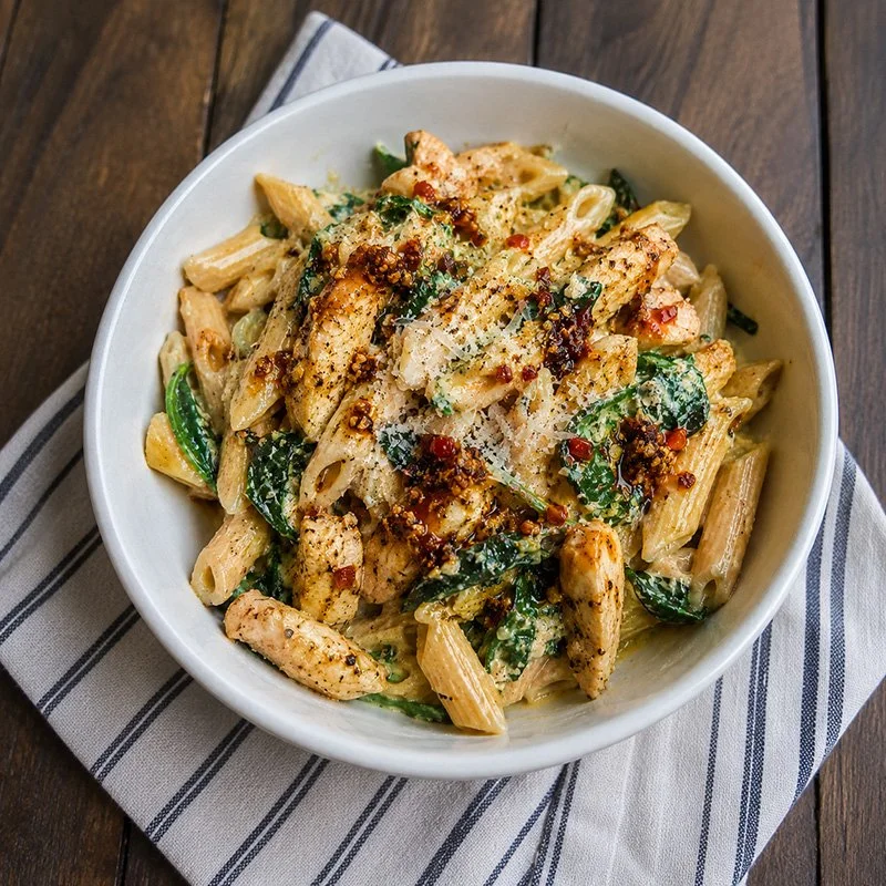 Protein pasta with chili crisp, chicken, spinach, parmesan, and a creamy high-protein sauce in a bowl.