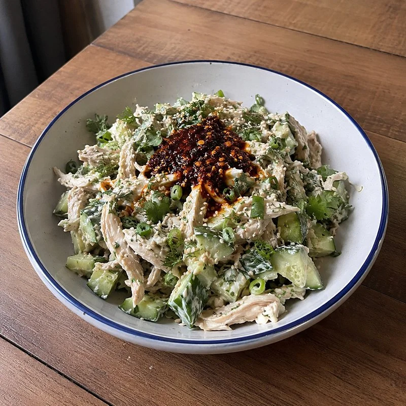 Healthy chicken cucumber salad with chili crisp, shredded chicken, cucumber, green onion, herbs, sesame seeds, and creamy spicy dressing in a bowl.