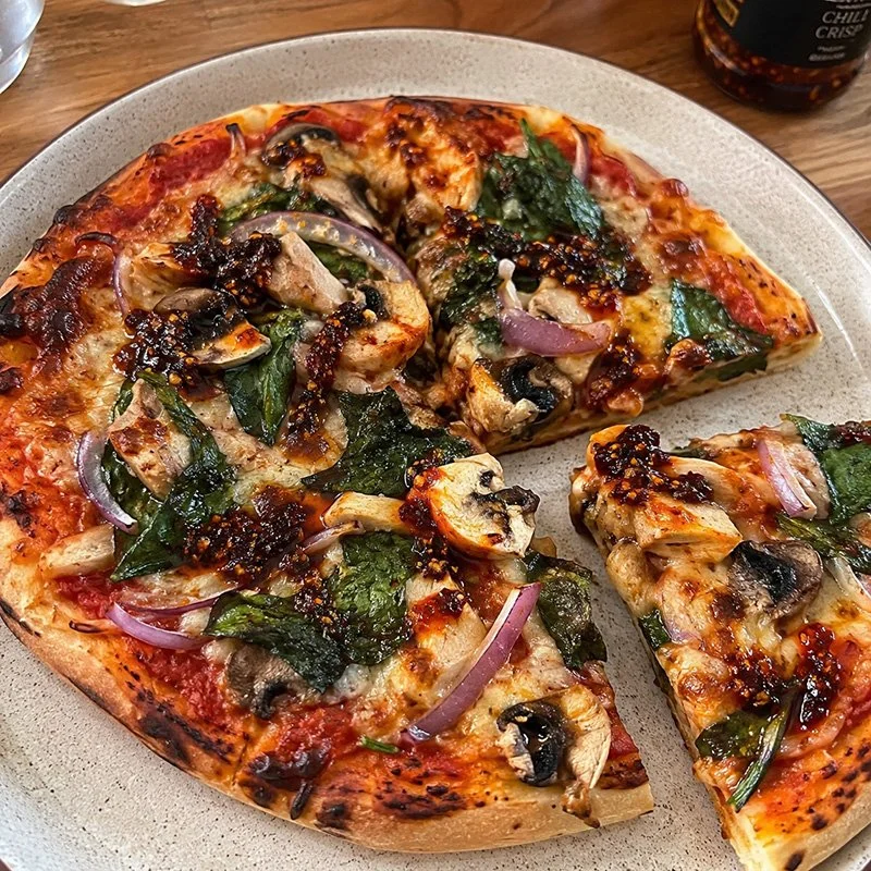 Healthy pizza with chili crisp, chicken, spinach, mushrooms, red onion, mozzarella, and spicy chili crisp on a homemade crust.