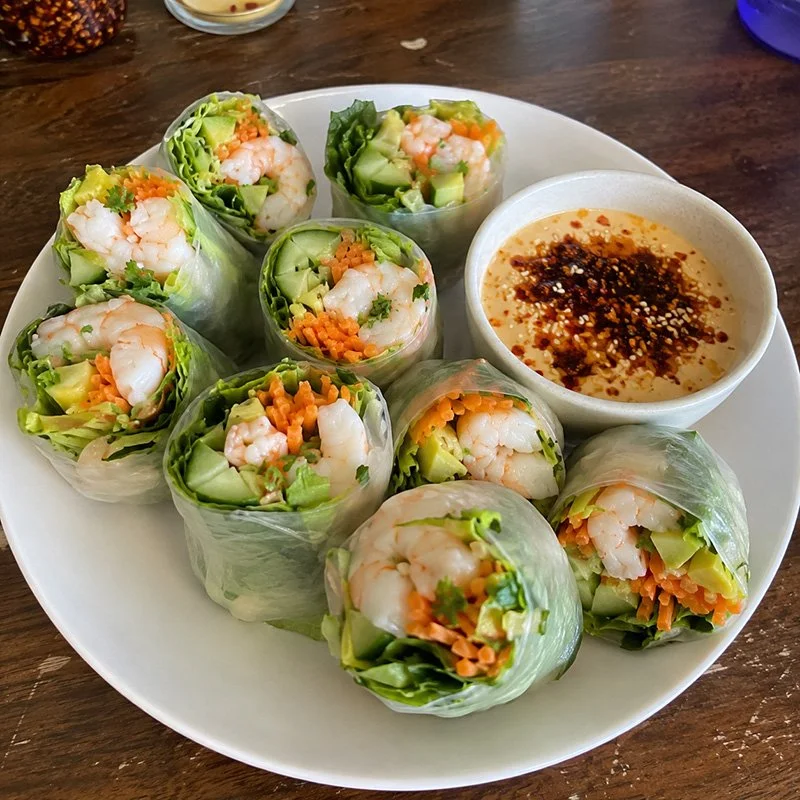 Healthy shrimp rice paper rolls with chili crisp, fresh vegetables, herbs, sesame seeds, and creamy spicy dipping sauce.