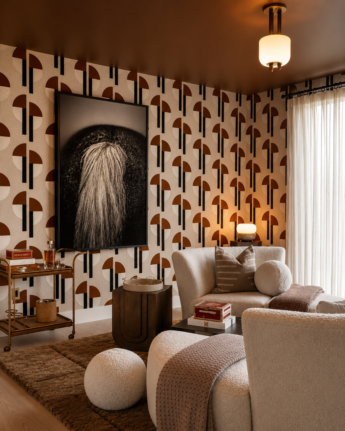 Living room with geometric patterned wallpaper, a large black-and-white portrait on the wall, a cream-colored sofa with pillows, a small side table with a lamp, and a window with sheer curtains.