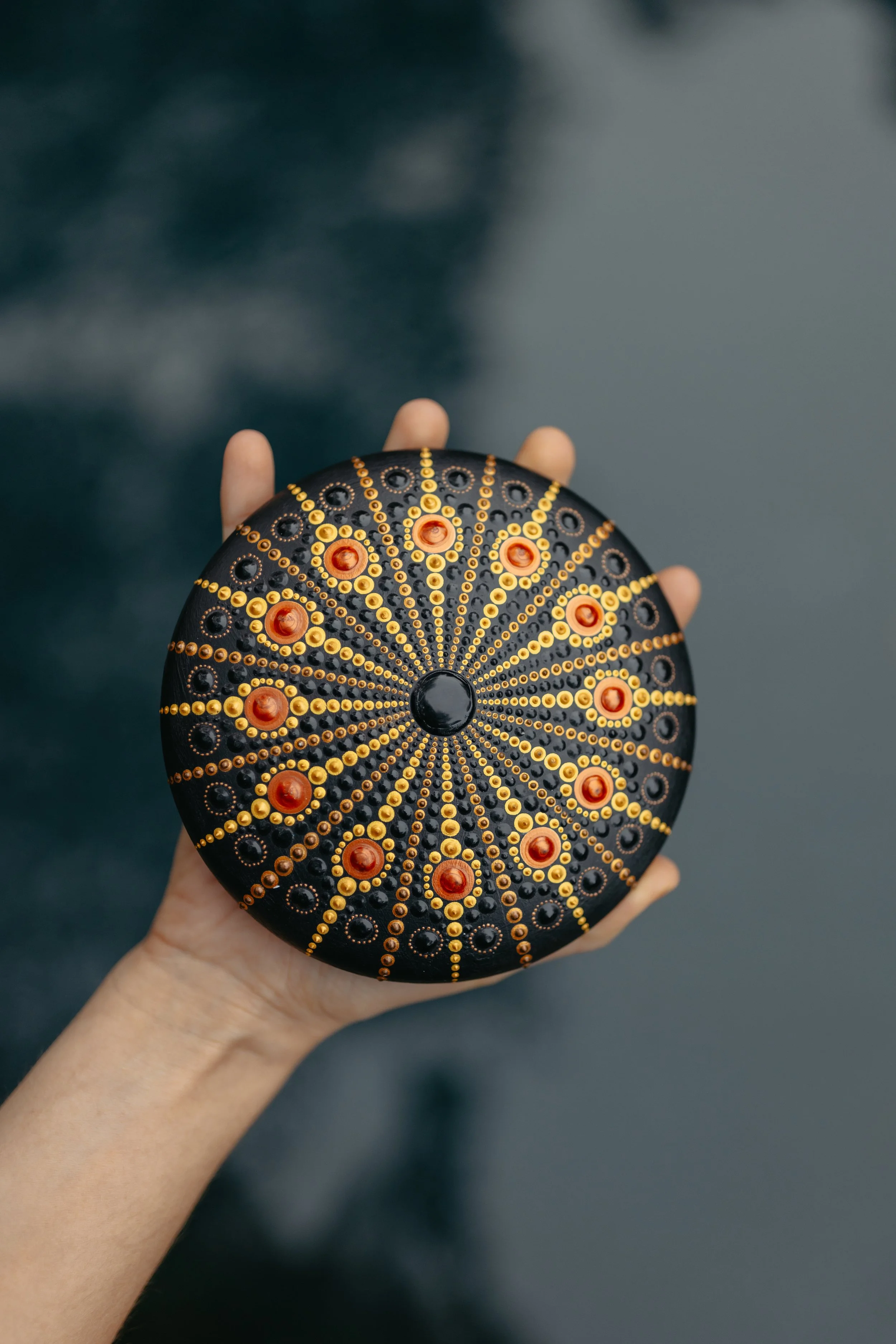 Person holding a black and orange decorative object with geometric patterns and circular designs.