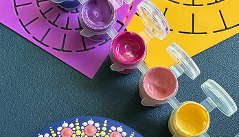Set of four small open containers with paint in purple, pink, peach, and yellow, placed on a multicolored background with purple and yellow paper cutouts.