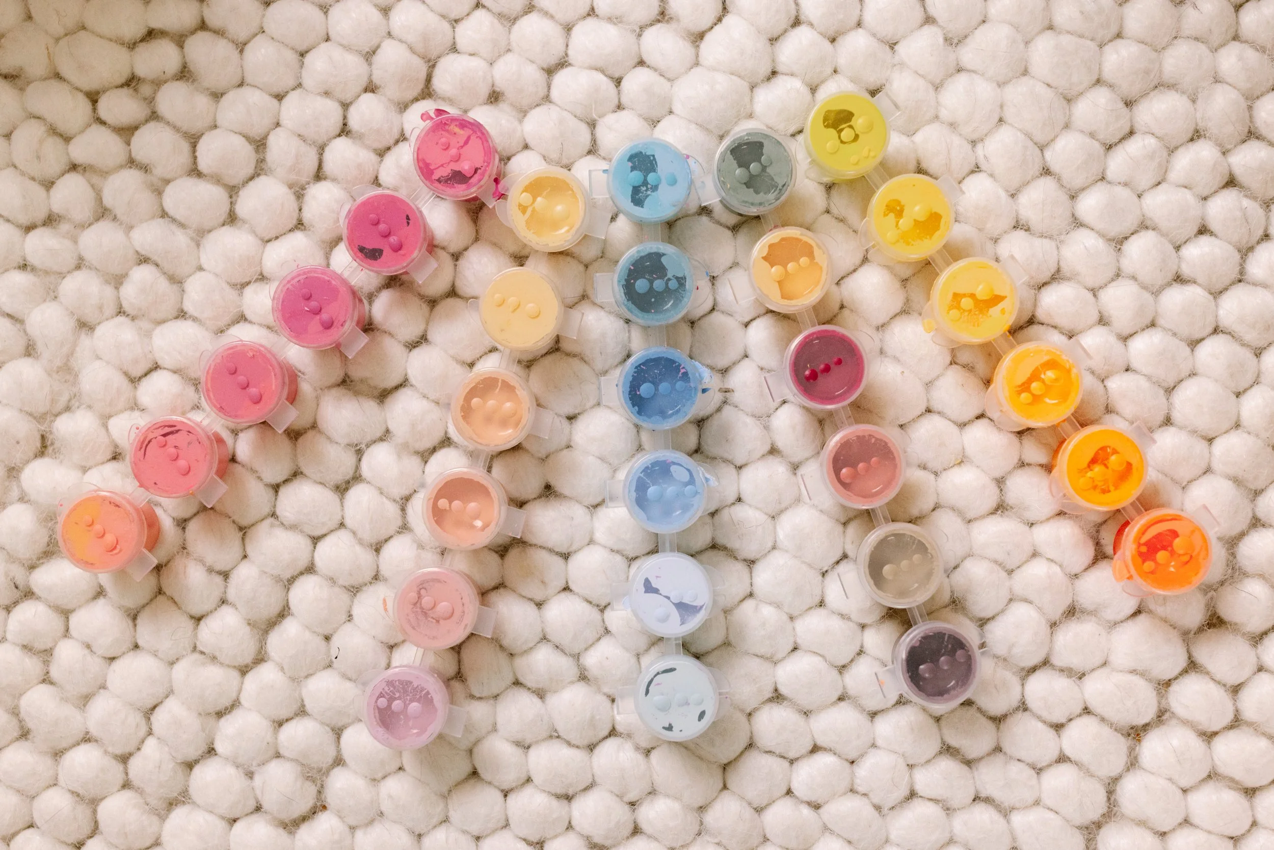 Colorful paint containers arranged on a fluffy white surface.