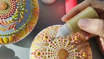 Person decorating a decorated cookie with a tube of icing or edible paint, intricate designs on the cookie surface.