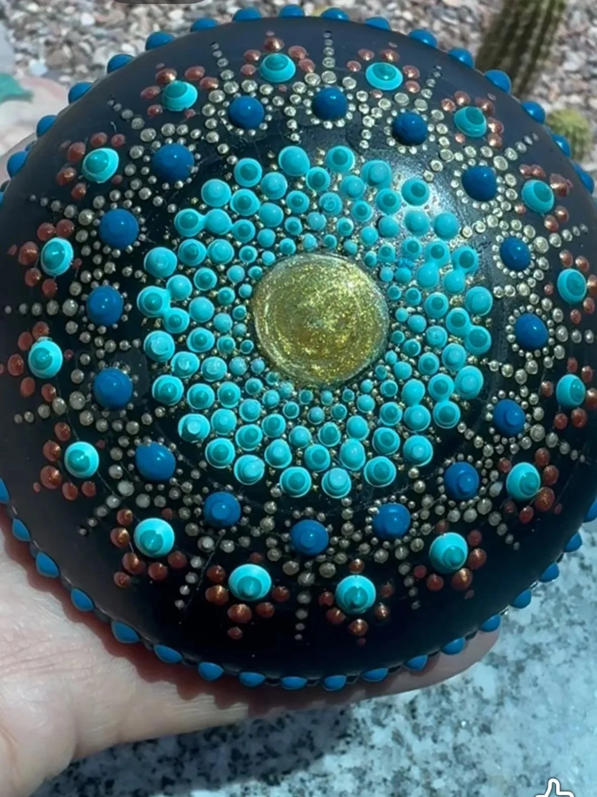 Decorated black rock with intricate pattern of turquoise, brown, and white beads arranged in a mandala-like design.