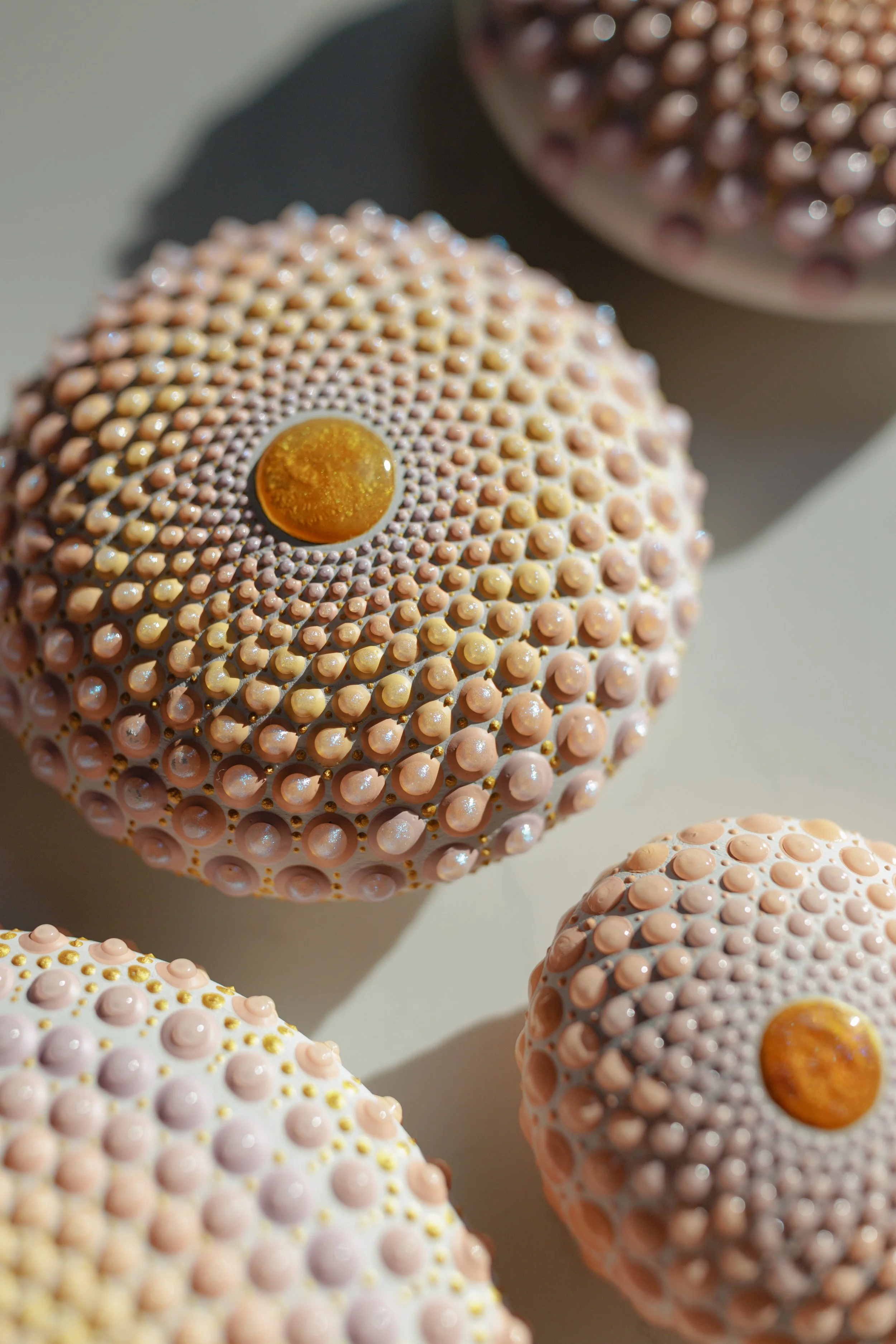 Close-up of decorative spheres with textured surface consisting of tiny, rounded bumps in pastel pink and peach colors, with a glossy, amber-colored center on each sphere.