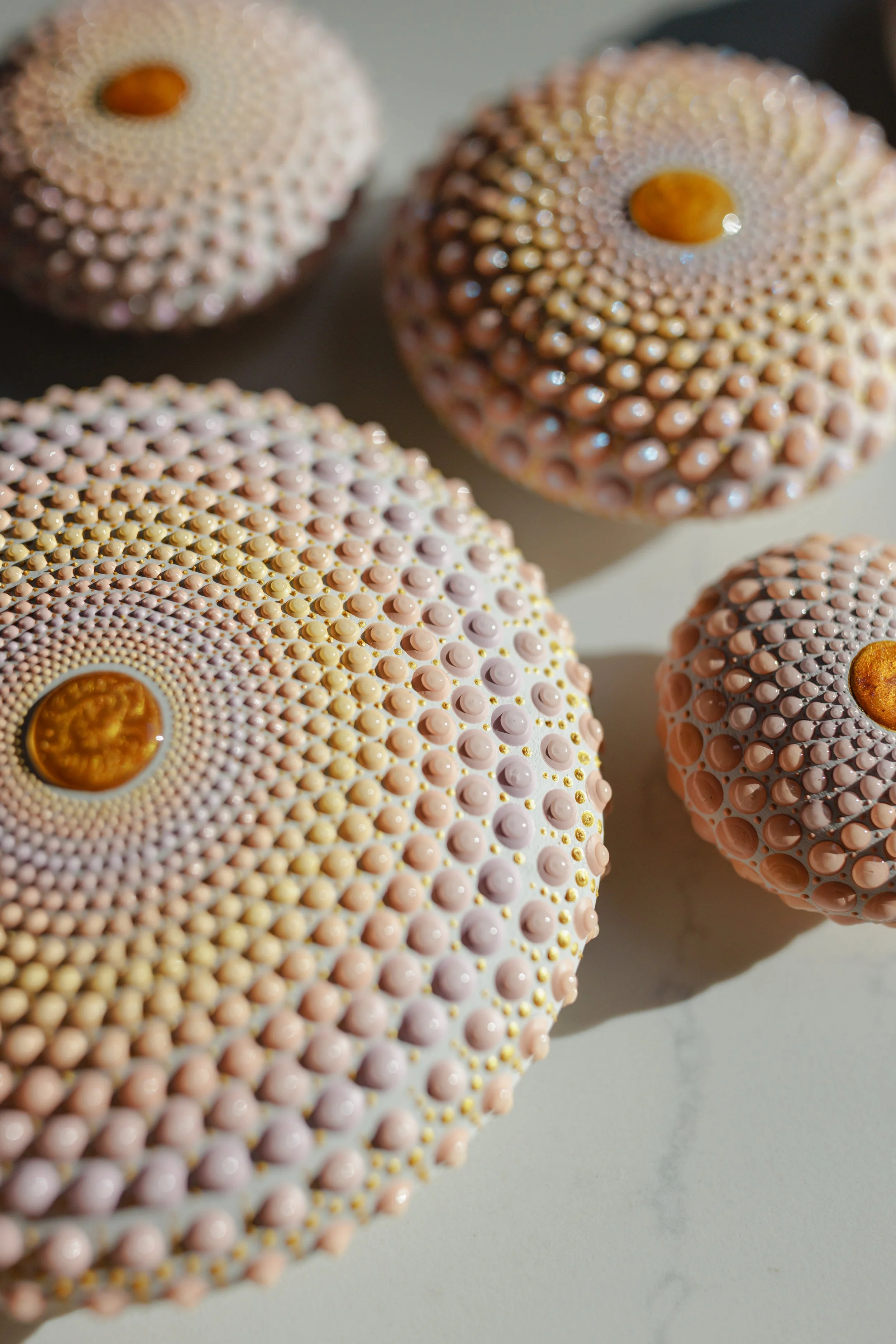Close-up of four decorative, textured spheres with small, rounded bumps and a central orange-colored detail, on a plain light surface.