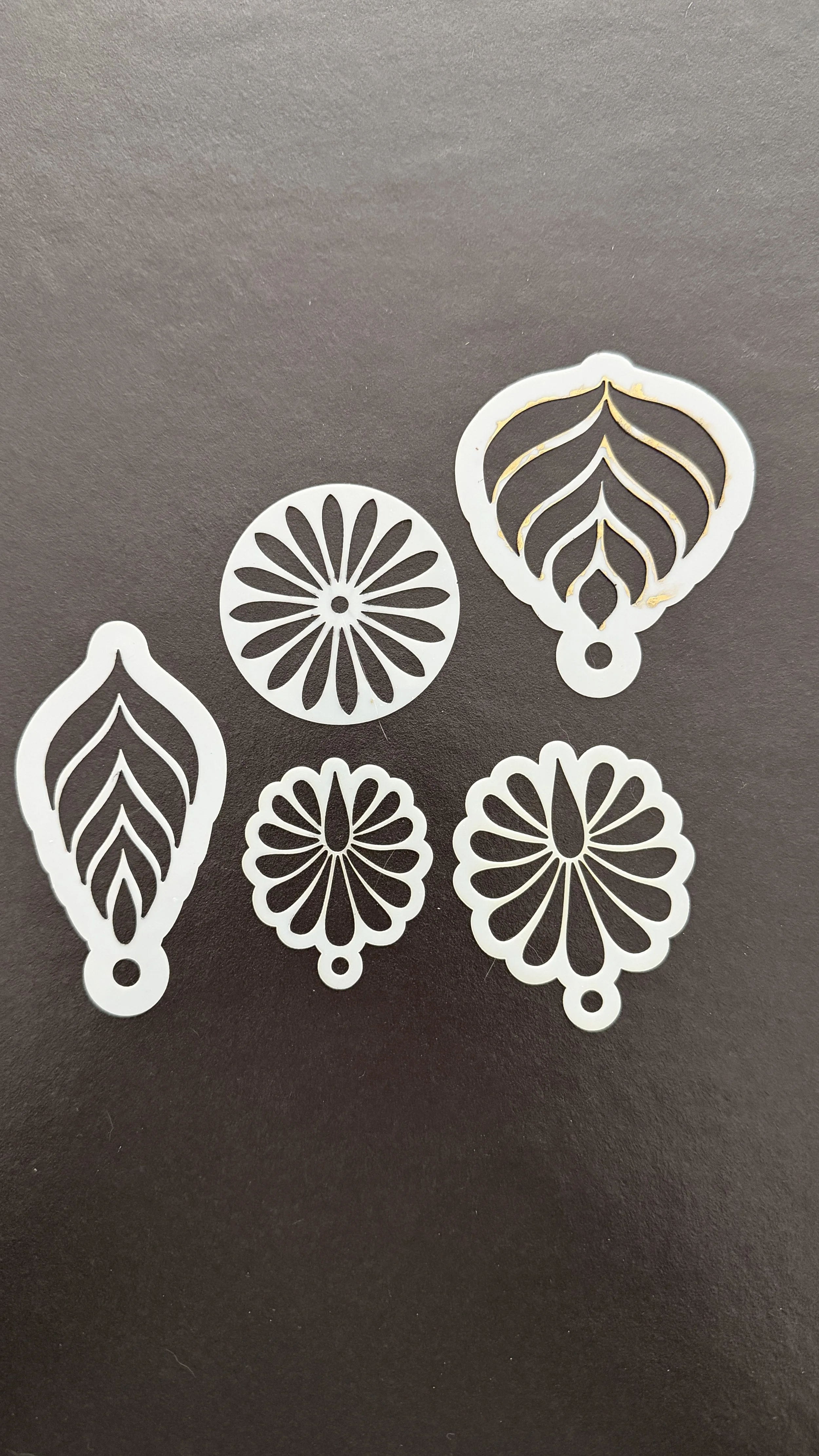 Set of six white paper cut-out ornaments with floral and leaf designs on a black surface.
