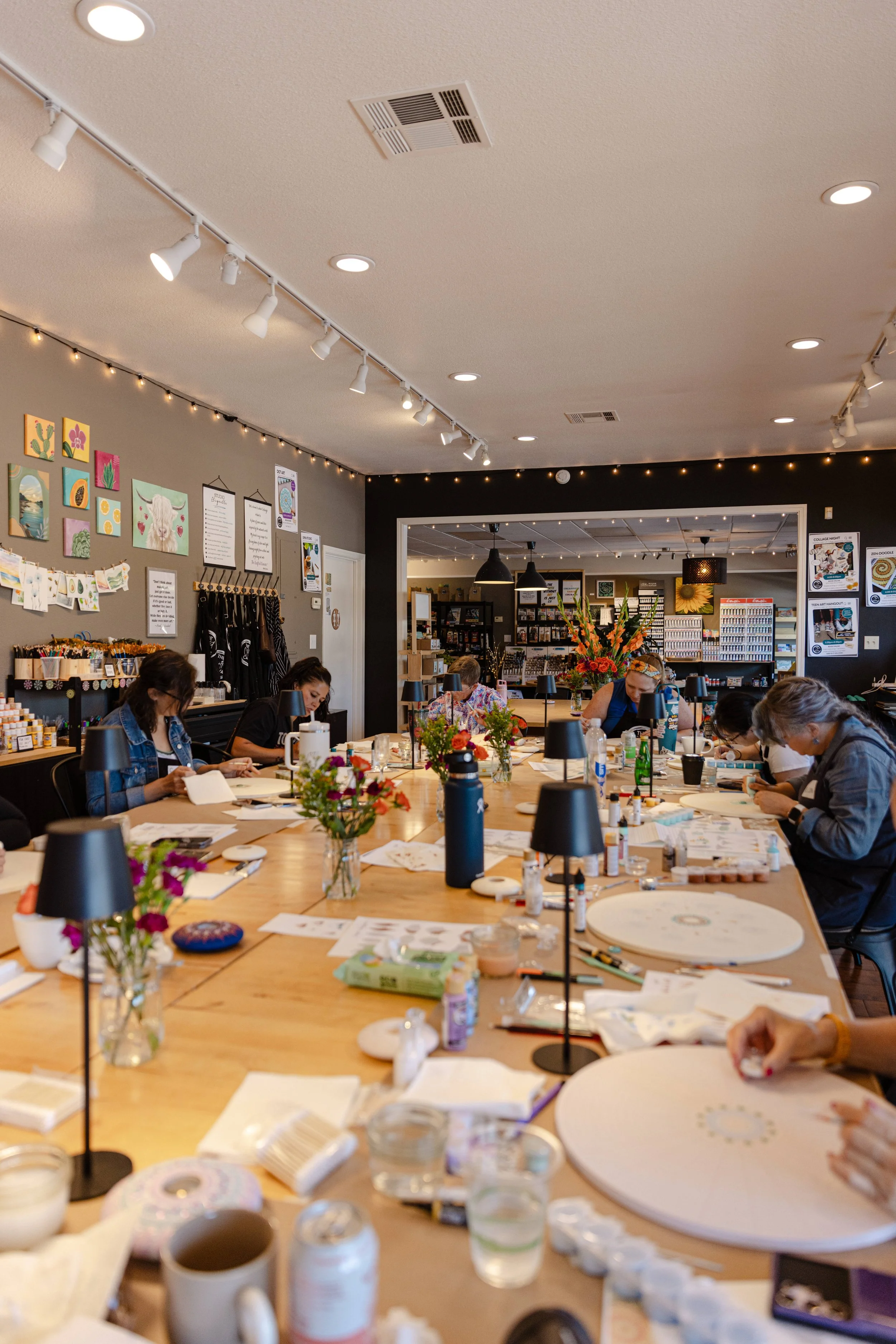 People seated around a large table on which various art supplies and decorations are spread, in an art workshop or class setting.