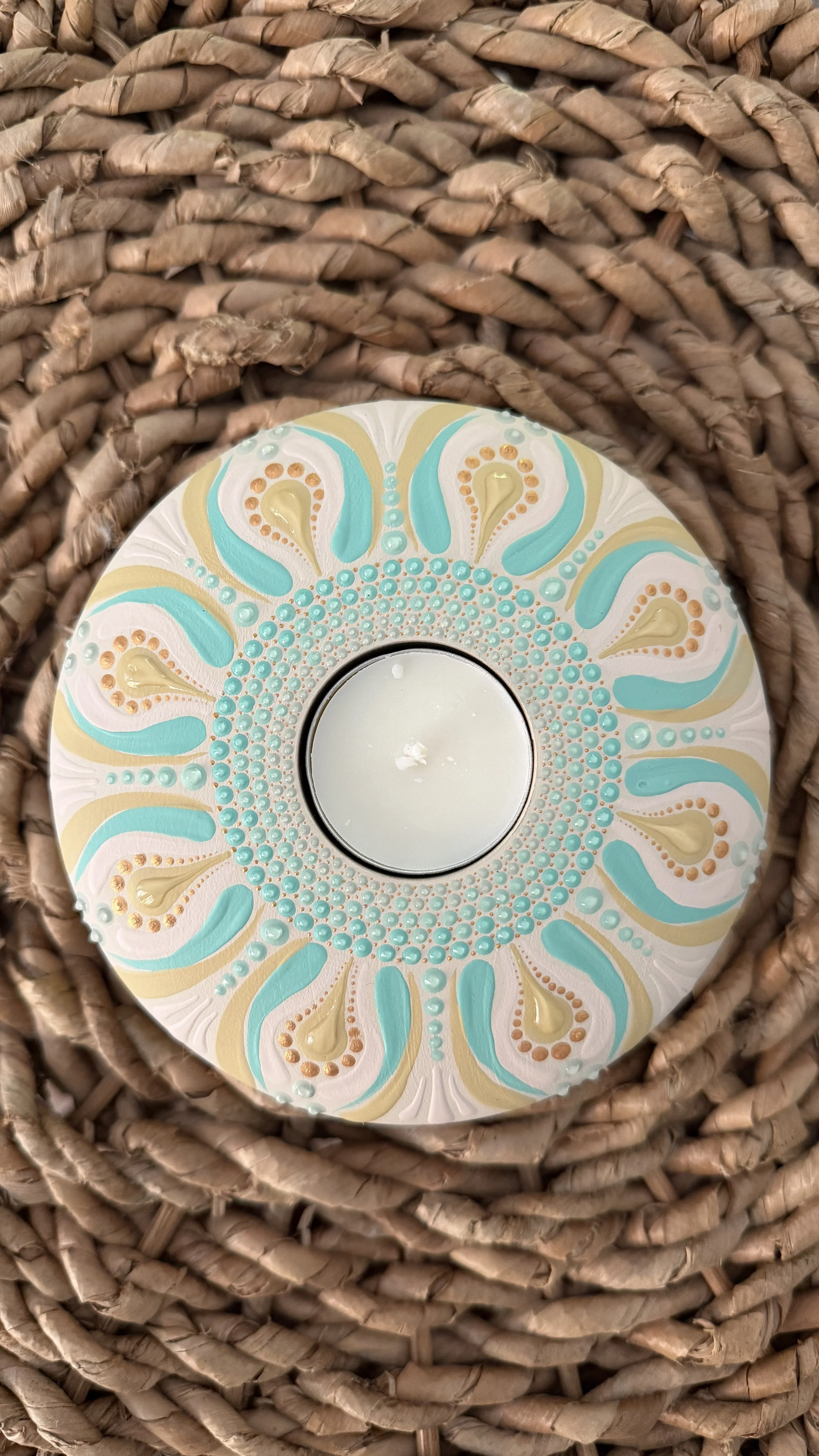 Decorative teal, beige, and white patterned coaster on top of a white candle in a woven basket.