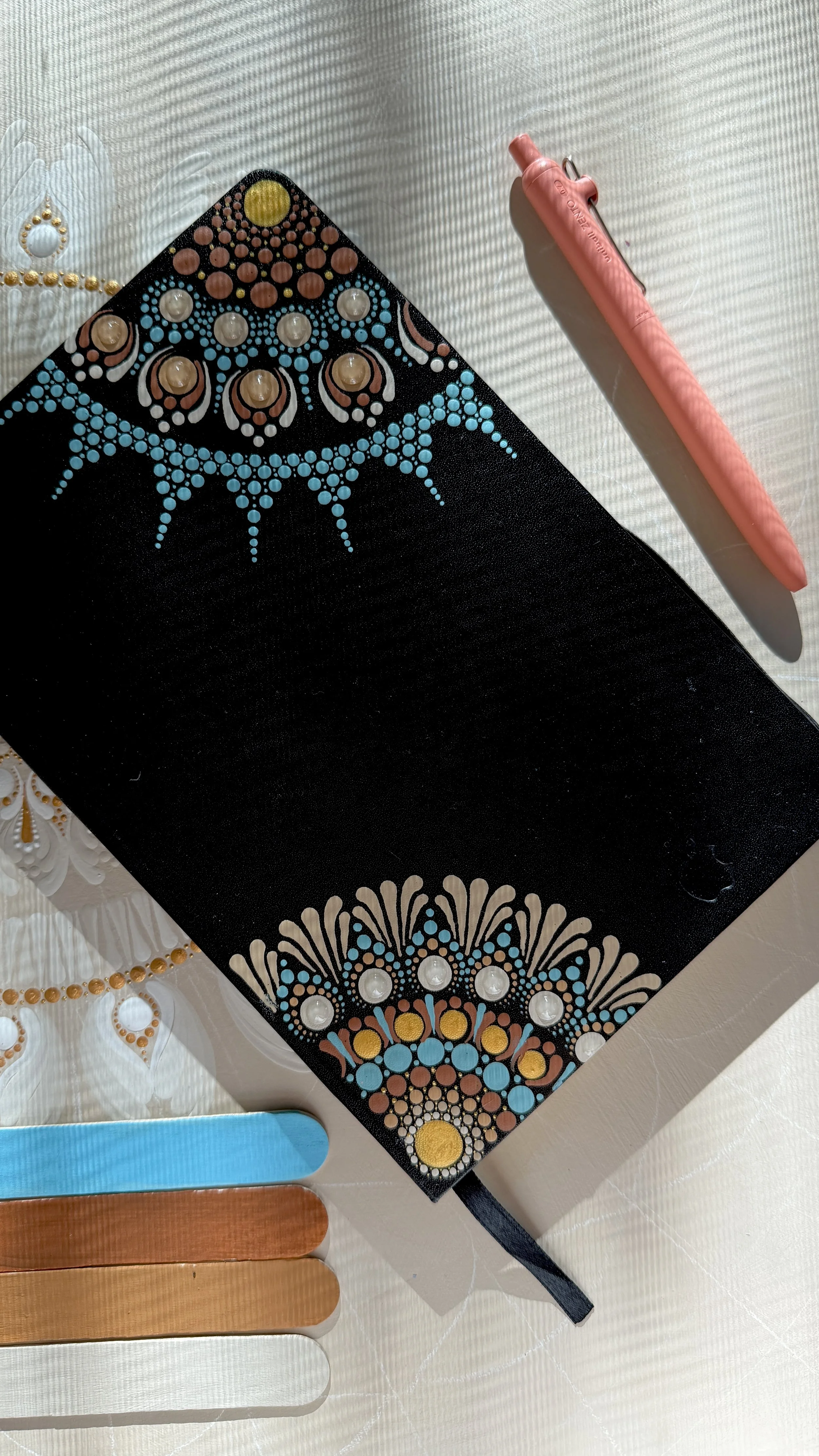 Close-up of a black portable speaker with decorative peacock feather design, next to a pink disposable razor and a palette of nail polish colors.