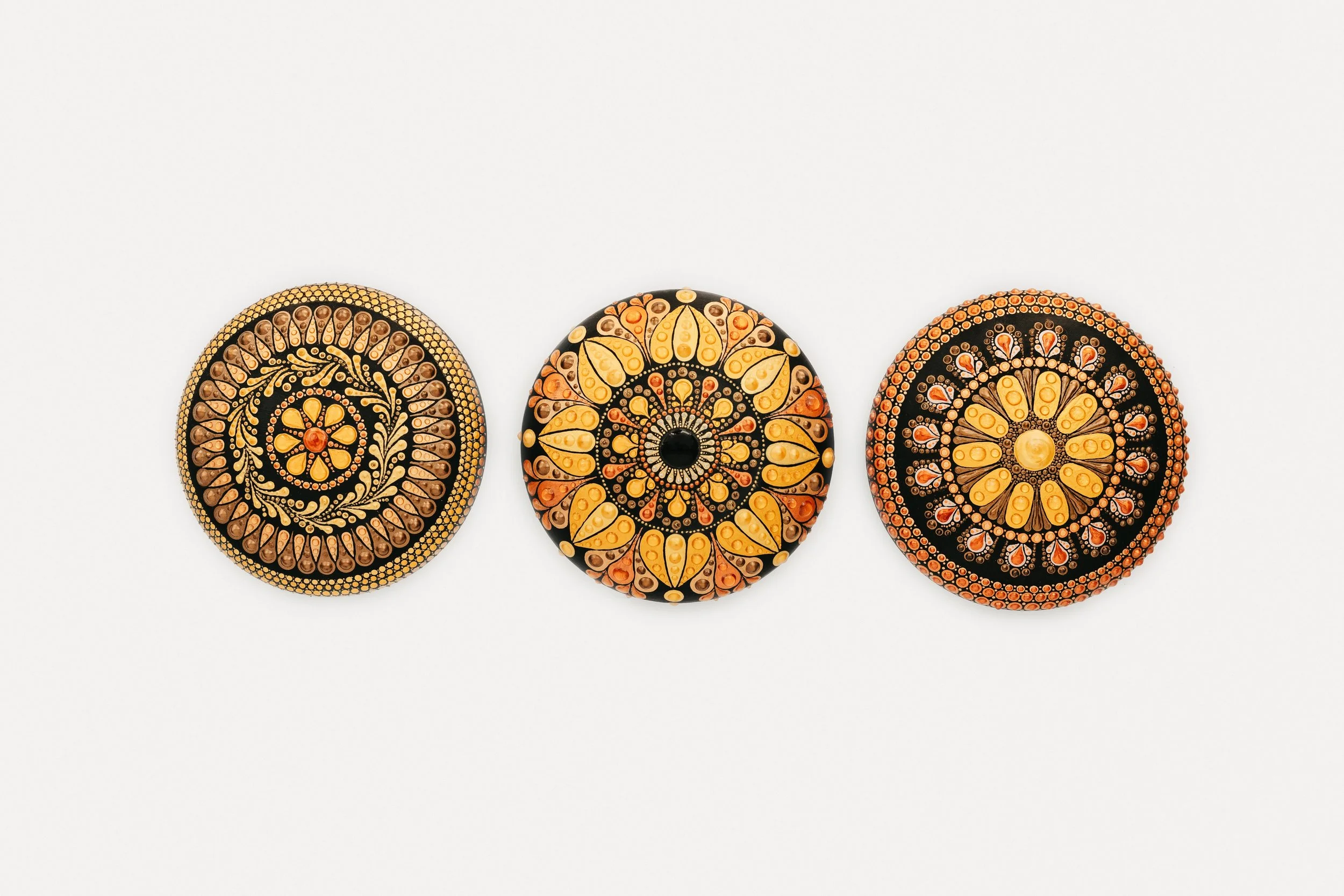 Three decorative circular objects with intricate patterns and warm colors, placed in a row on a white background.