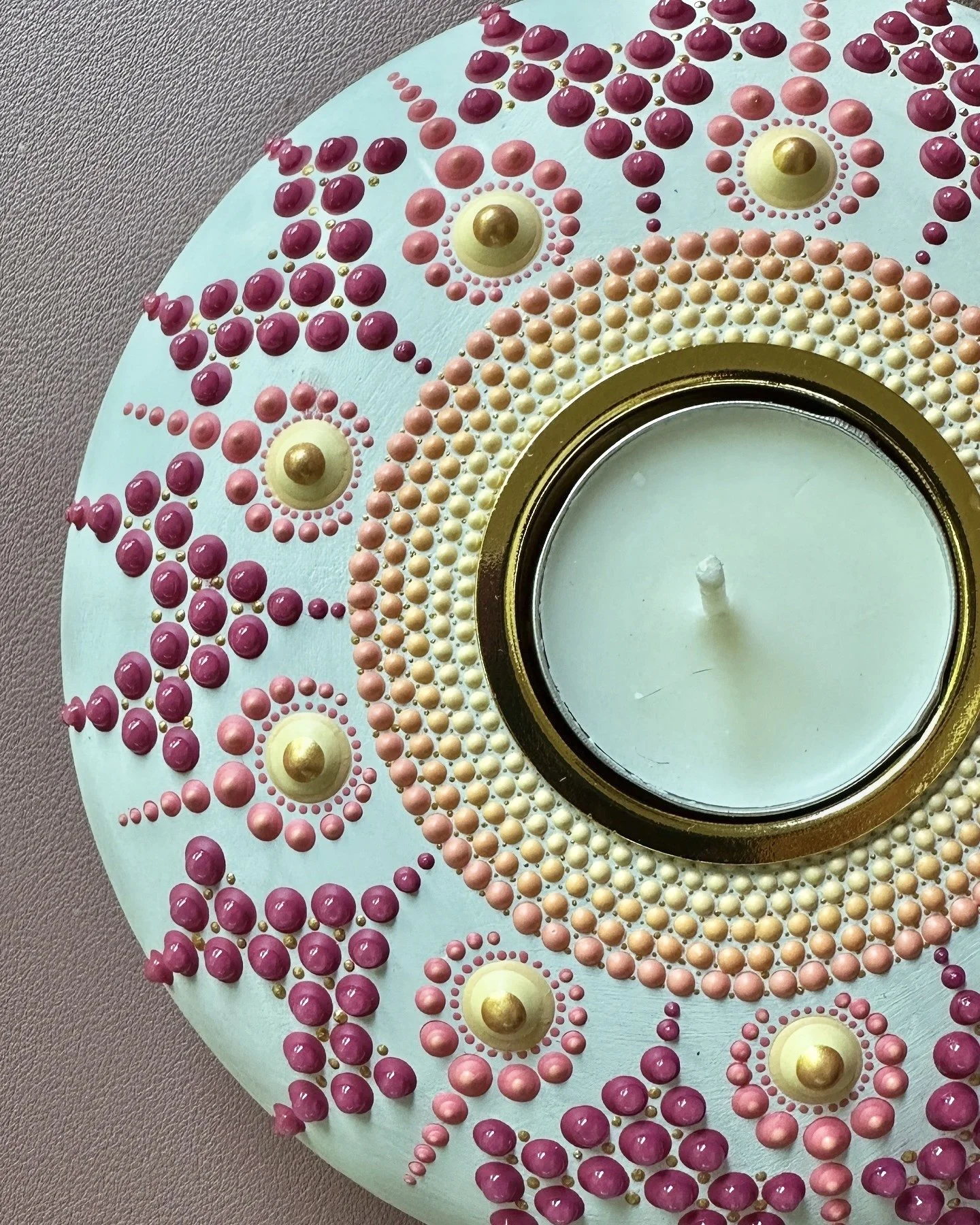 Decorated circular cake with pink, peach, and cream colored beads, gold accents, and a central candle.