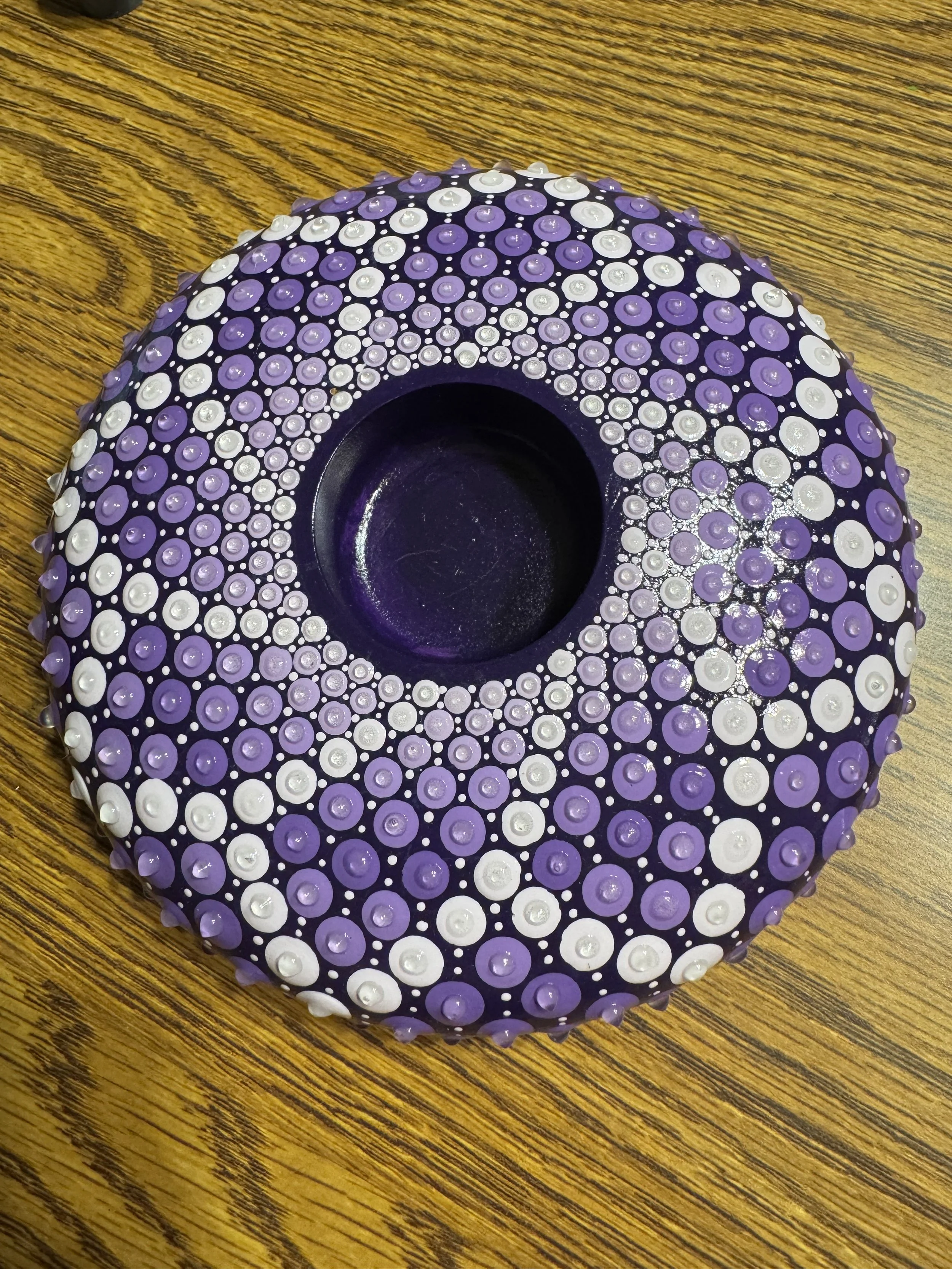 A decorative purple and white circular object with textured bumps, placed on a wooden surface.