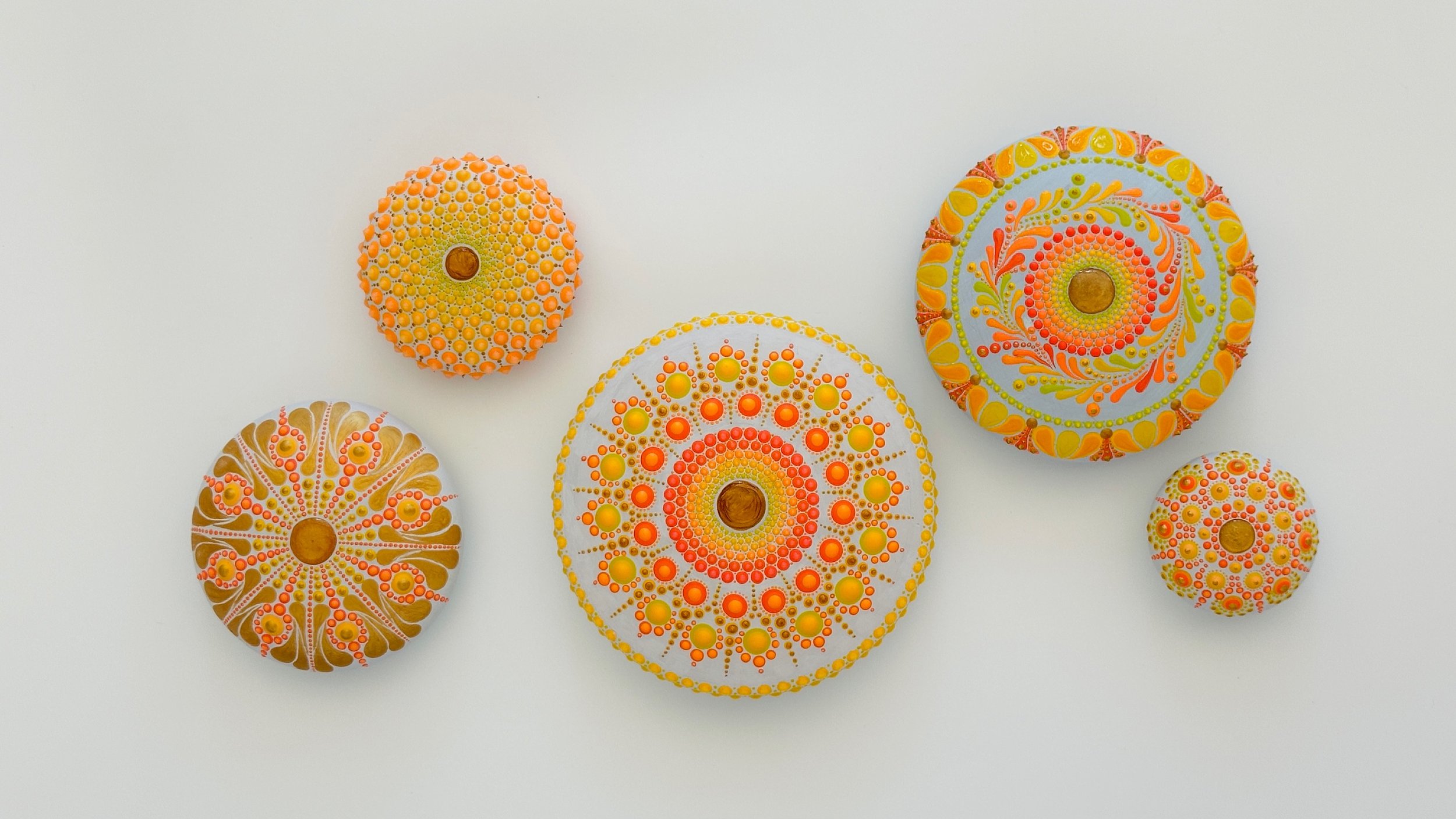 Colorful decorative stones with intricate dot patterns in shades of orange, yellow, and white, arranged on a white background.